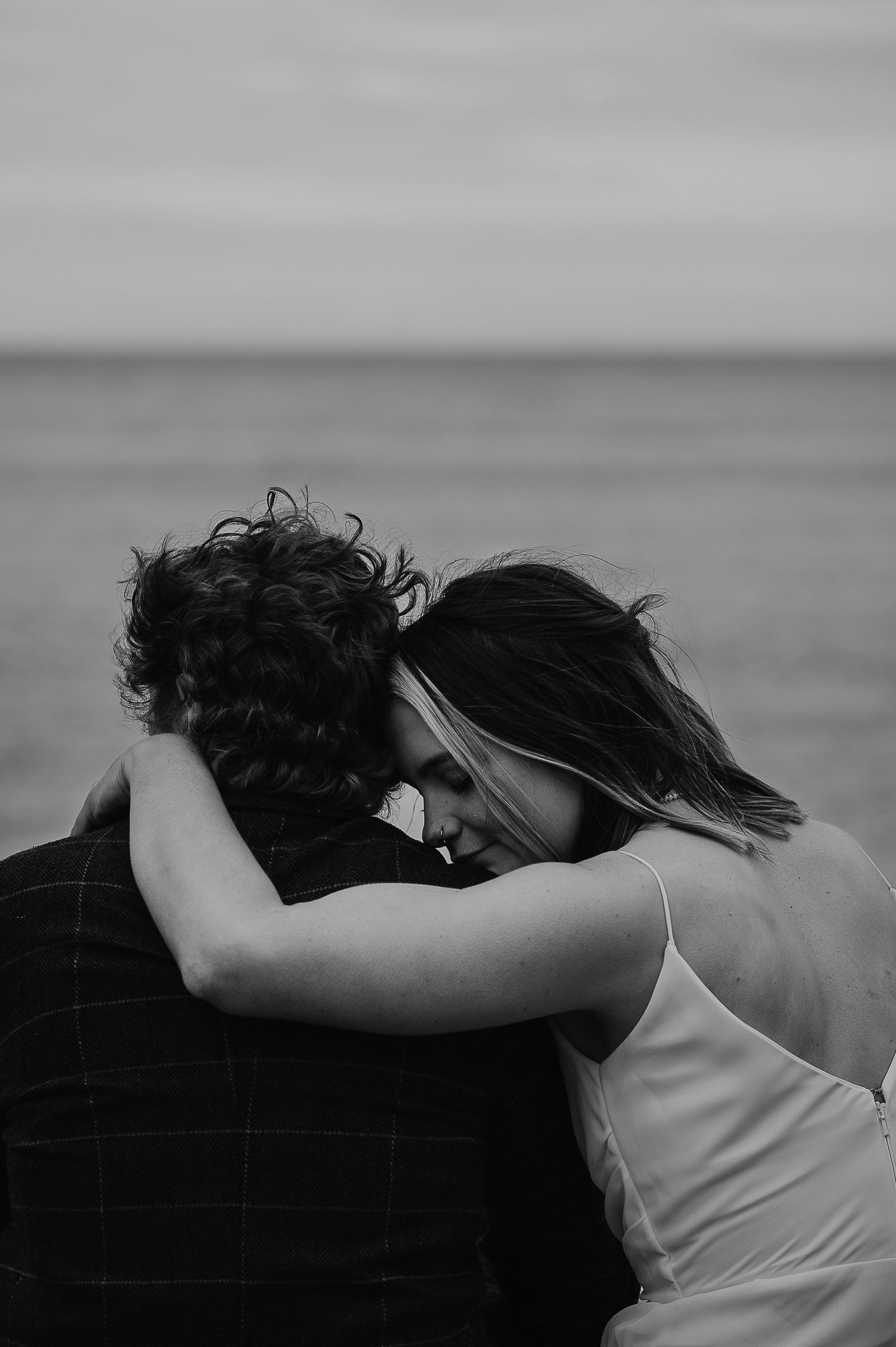 A romantic black and white photo of a couple embracing while looking out at the ocean.
