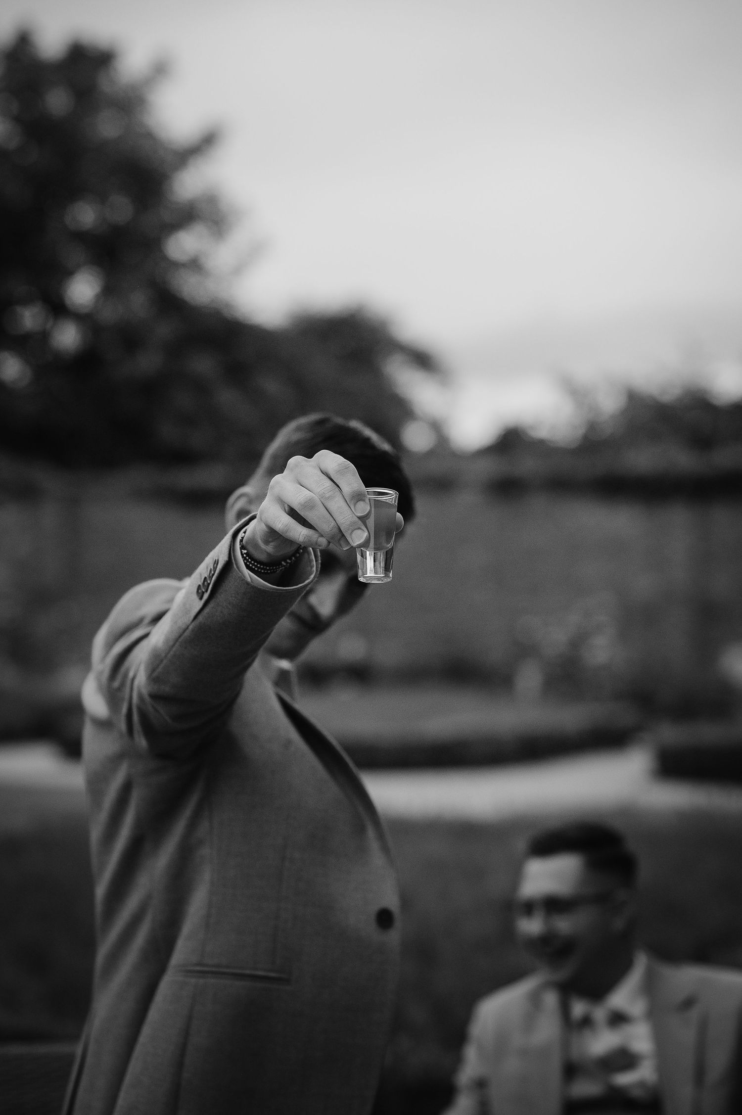A black and white image of someone holding up a shot glass during wedding celebrations.