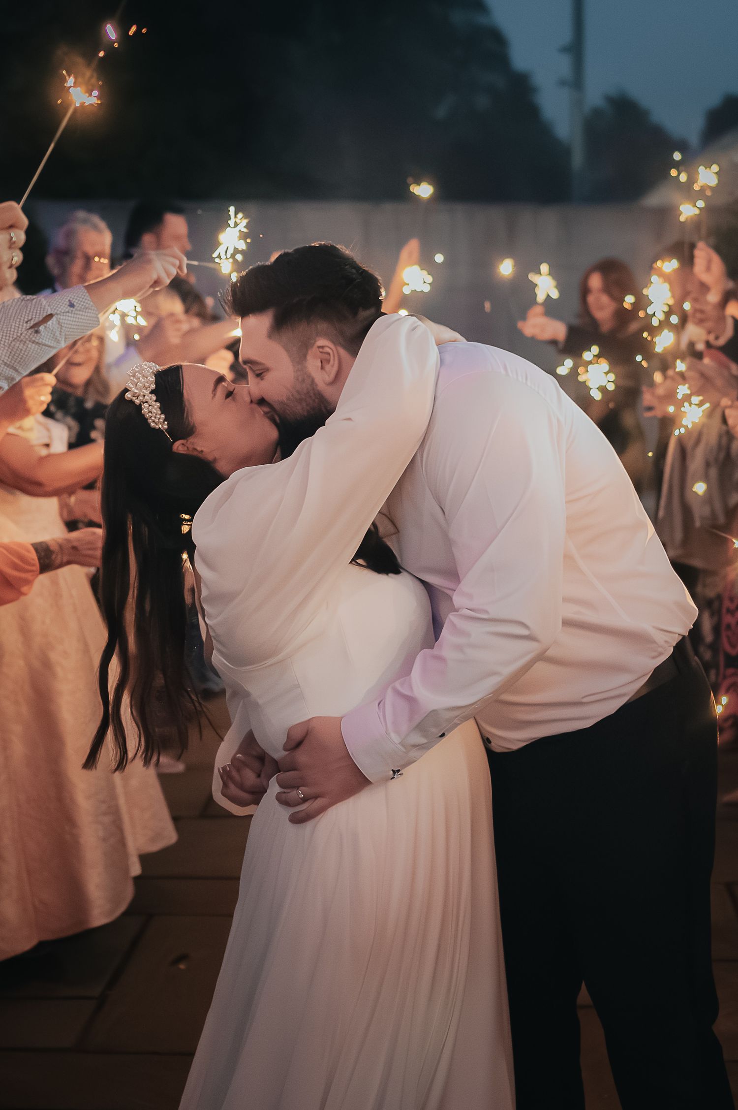 Romantic kiss during sparkler send-off at wedding reception.