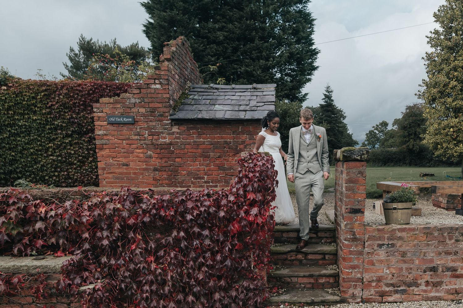 A couple descending brick steps covered with red autumn ivy at an outdoor venue.