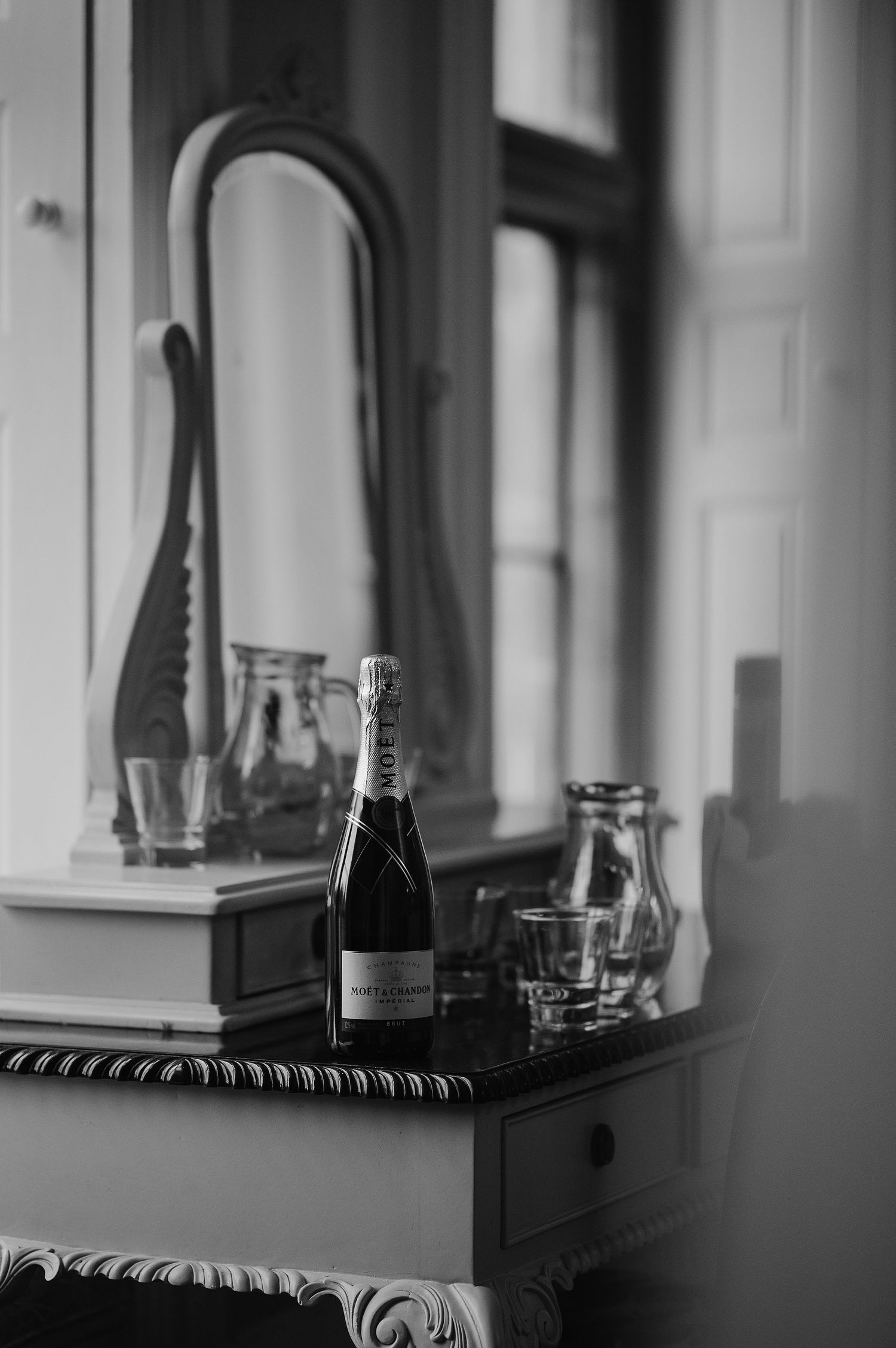 Black and white photo of champagne bottles and glasses on an elegant vanity table.