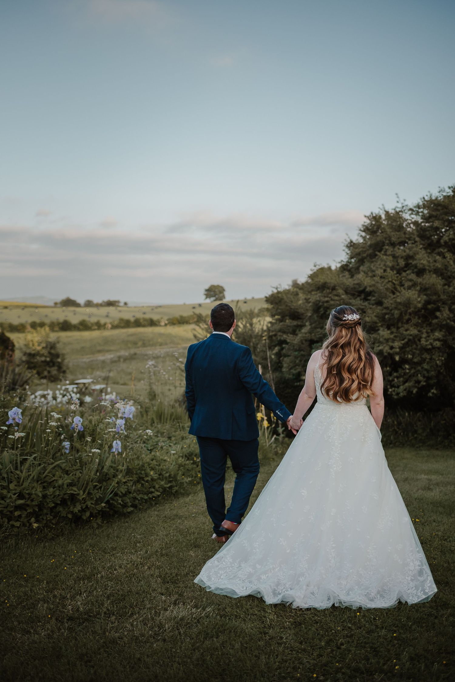 A couple stands in a field at sunset overlooking rolling hills and countryside.