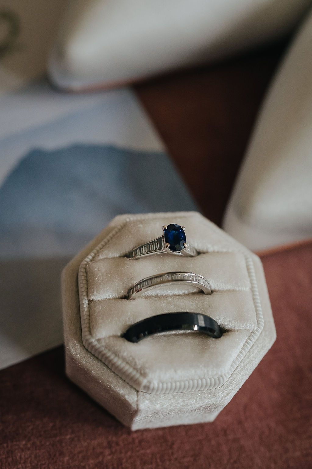 Three elegant wedding rings including sapphire engagement ring displayed in cream hexagonal box.
