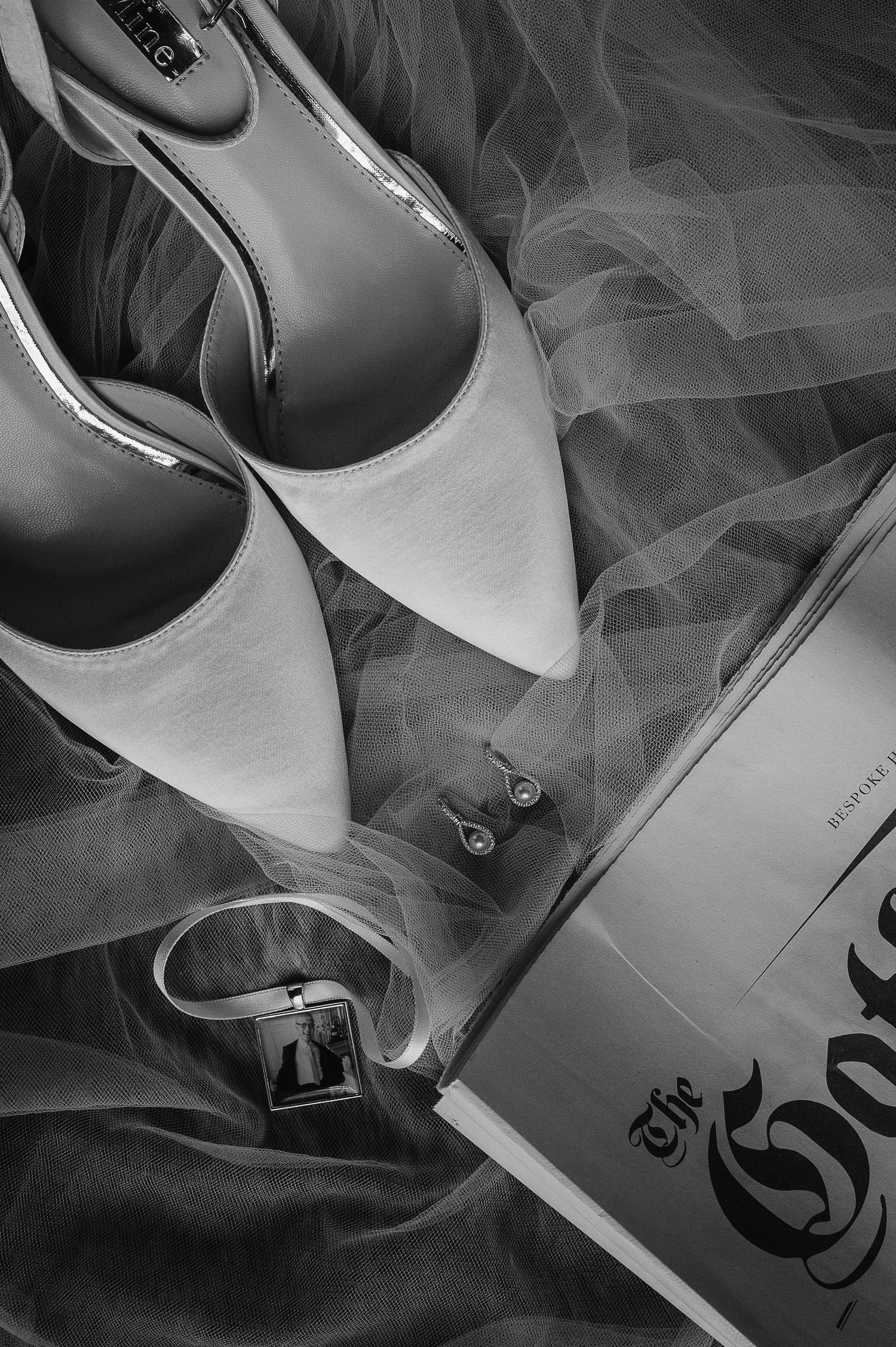 Wedding accessories including white shoes, veil, and rings arranged on light surface.