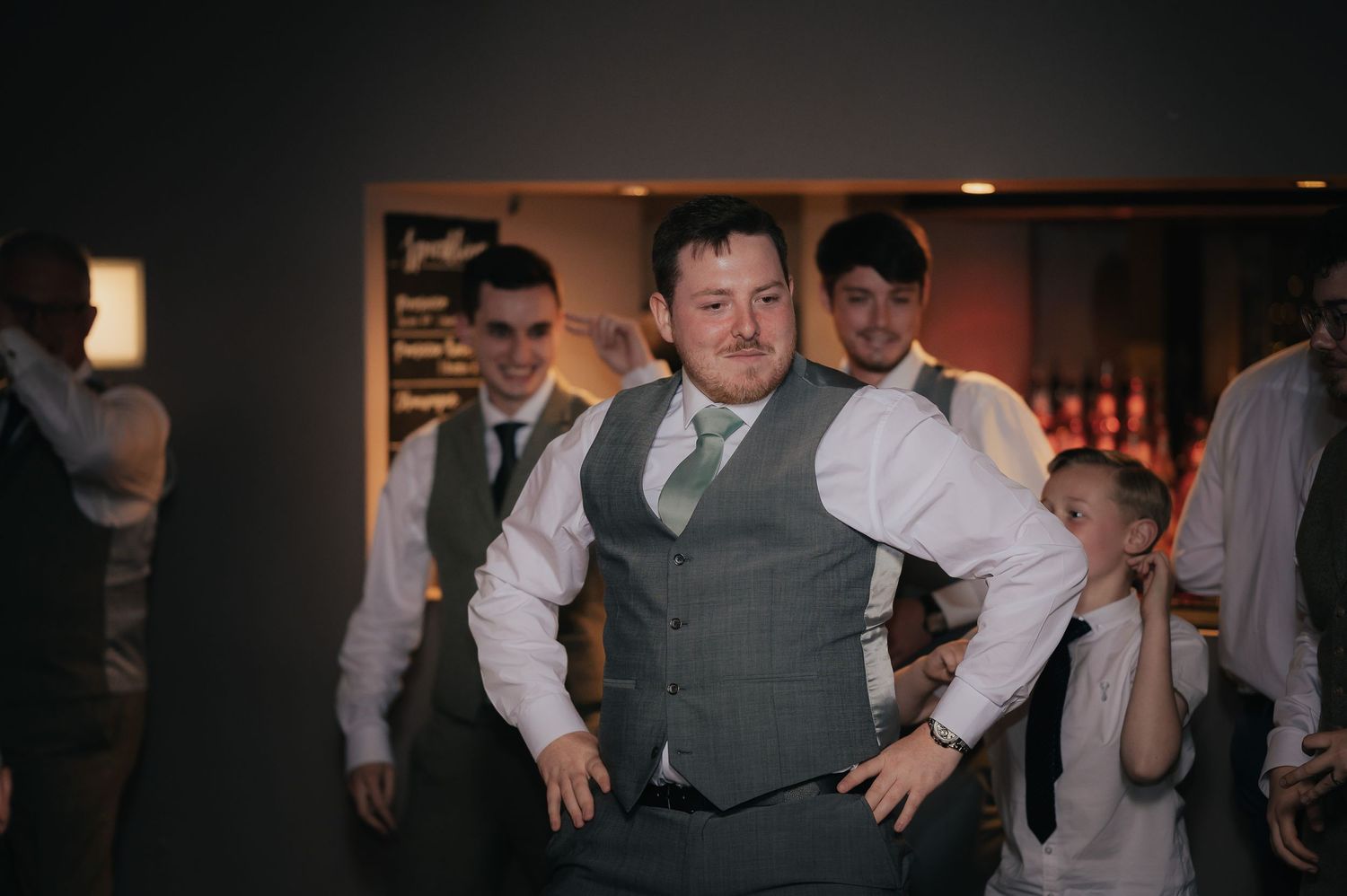 Groomsman in formal attire performs dance moves at wedding reception.