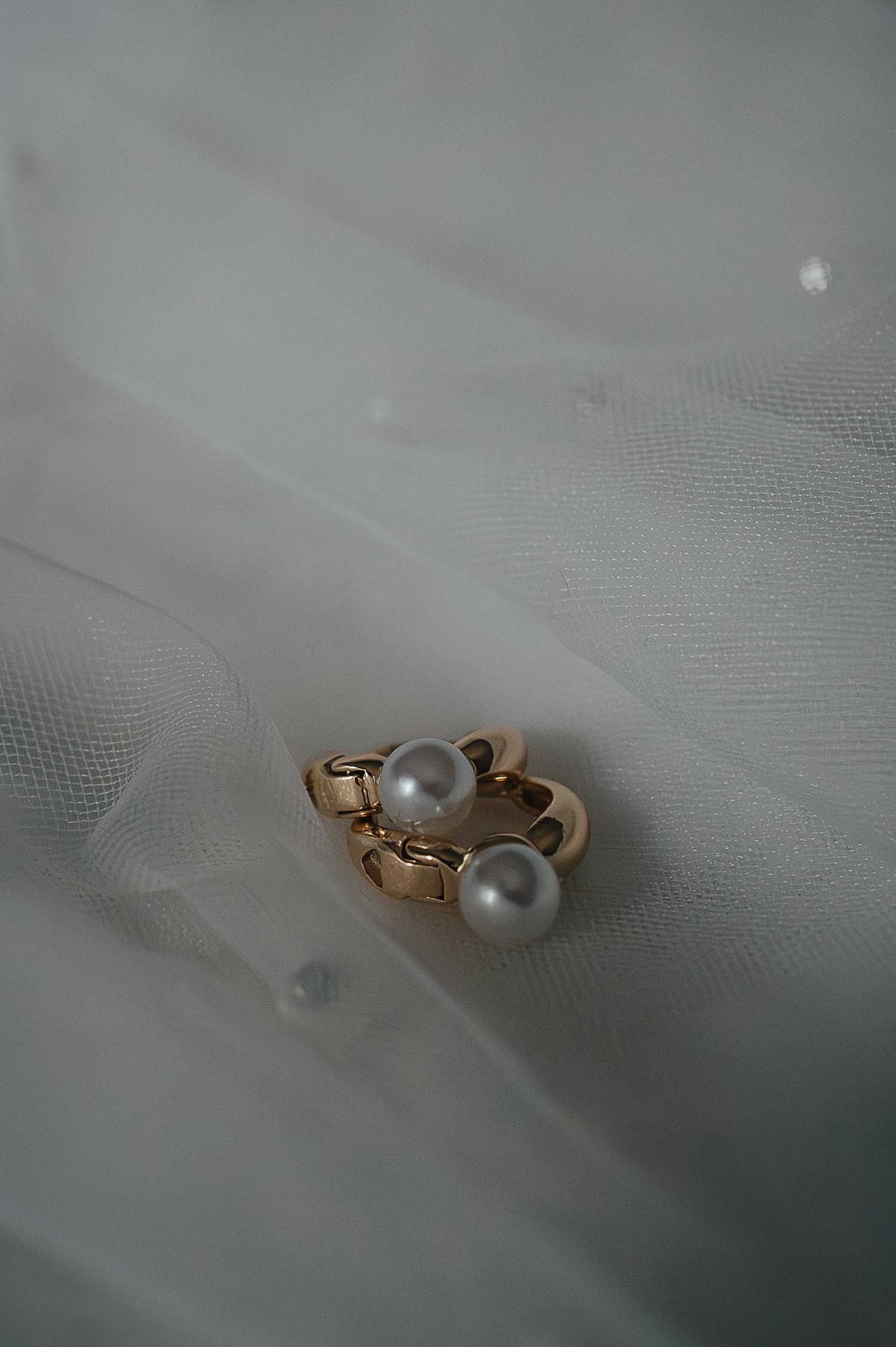 Gold pearl ring sitting on delicate white tulle fabric in soft lighting.