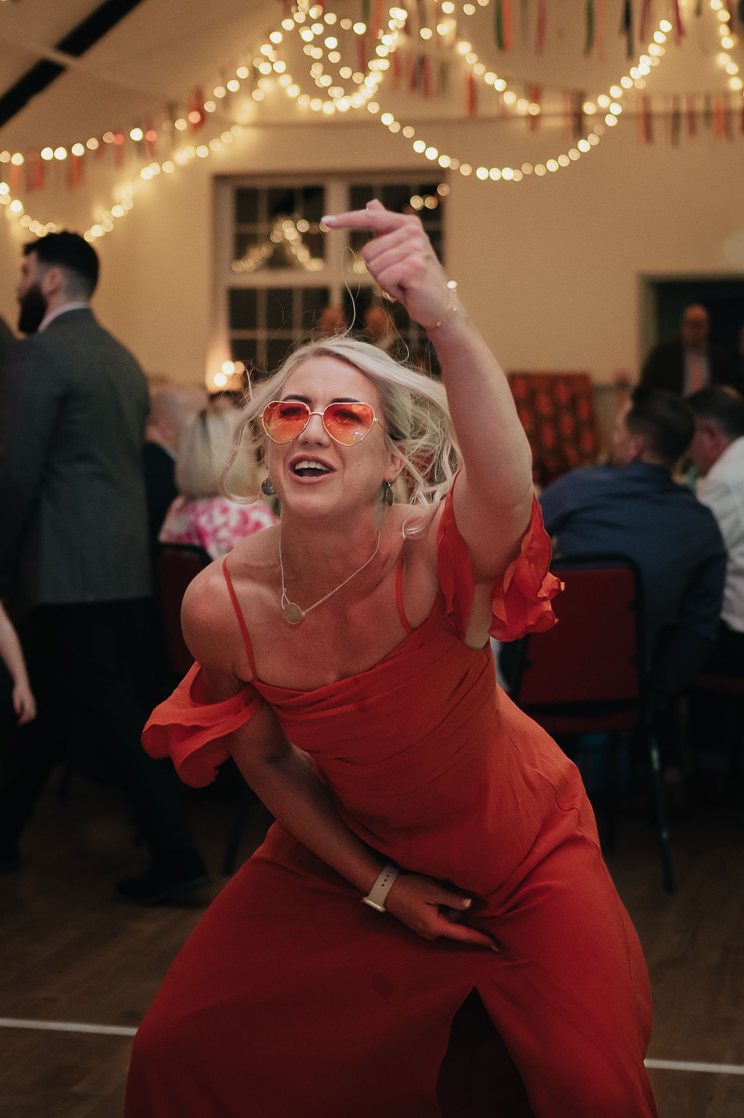 A woman in a red dress dances energetically under string lights at a party.