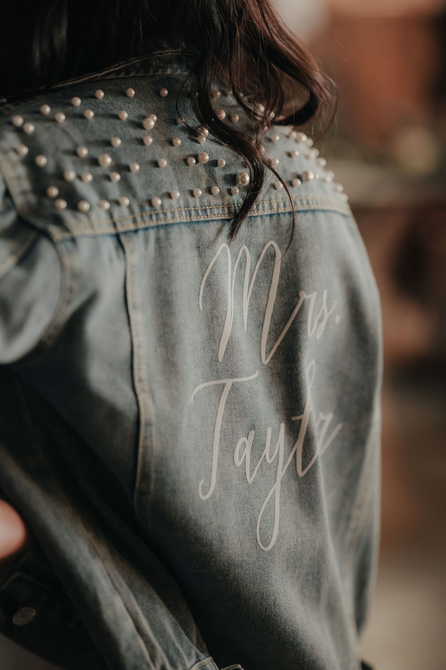 Close-up of a denim jacket with rhinestone embellishments and cursive text.