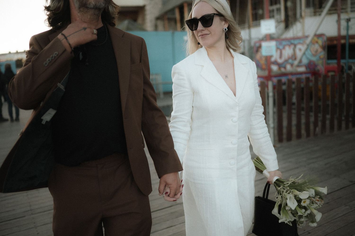 Couple in contrasting brown and white outfits walking together on a boardwalk.
