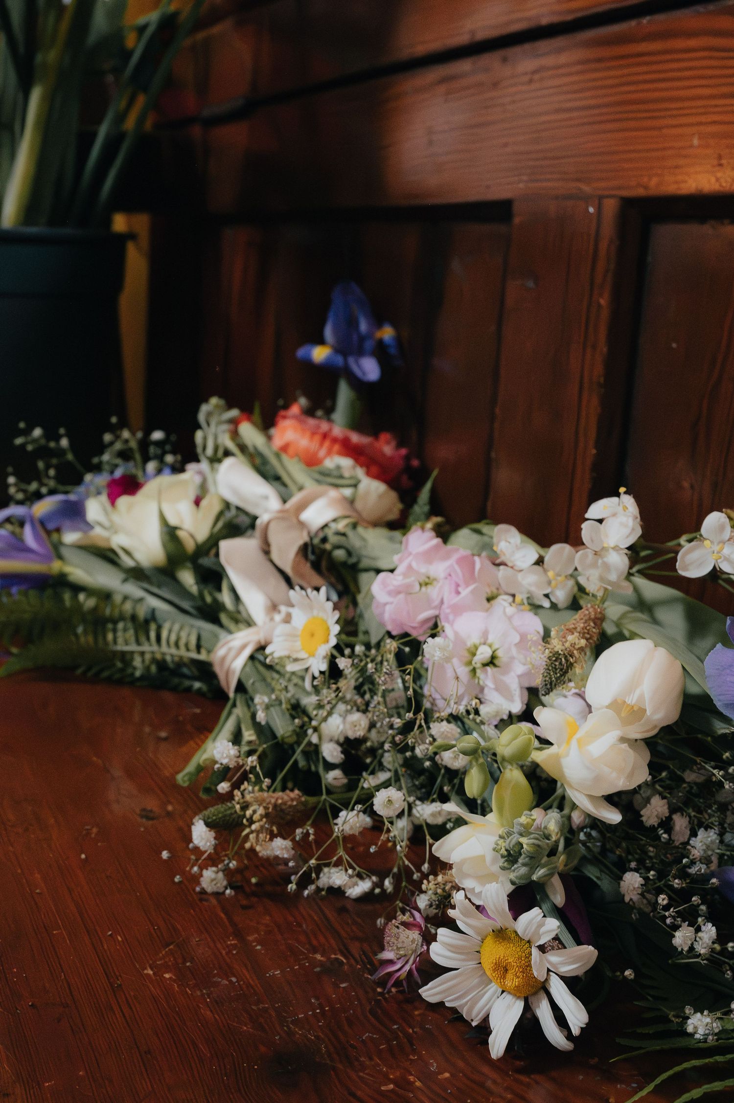 Delicate floral arrangement with daisies, orchids and baby's breath on wooden surface.