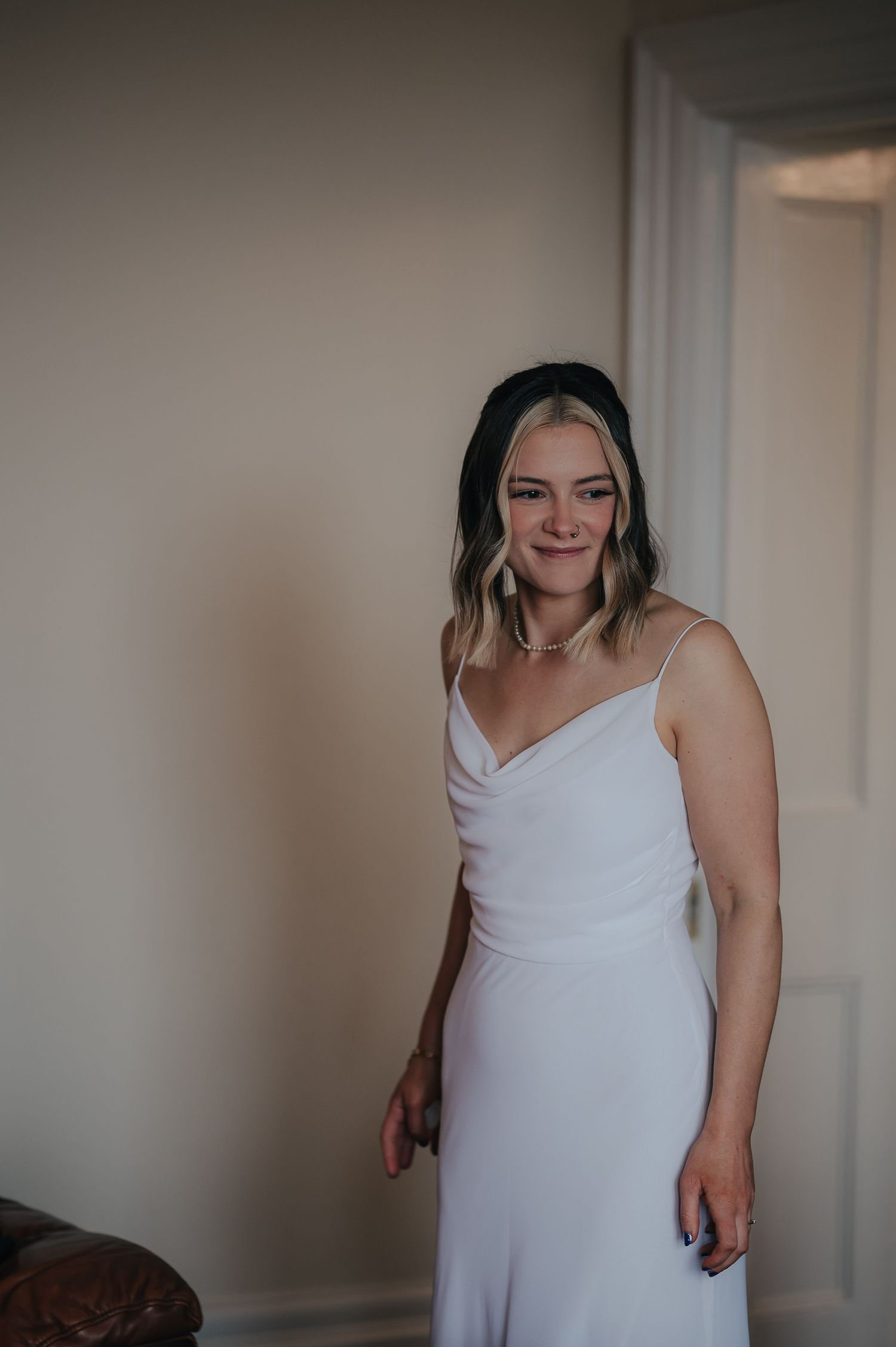 A person wearing a simple white cowl neck dress poses in an elegant indoor setting.