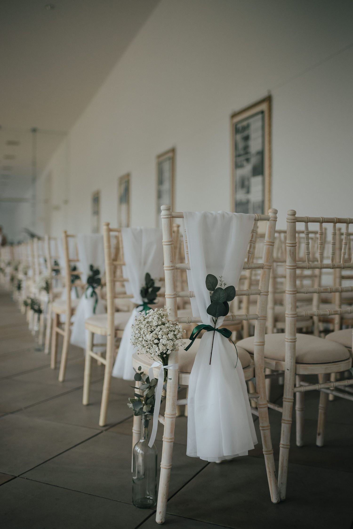 White Chiavari chairs lined up for wedding ceremony with delicate floral decorations.