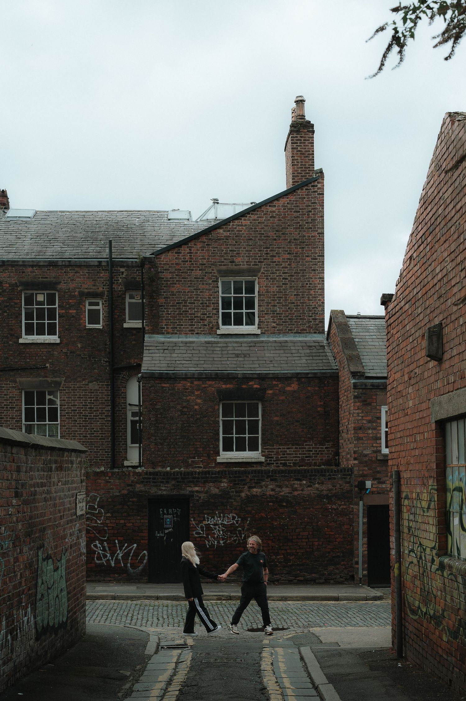 People walk along a narrow cobblestone alley between old brick buildings in an historic neighborhood.