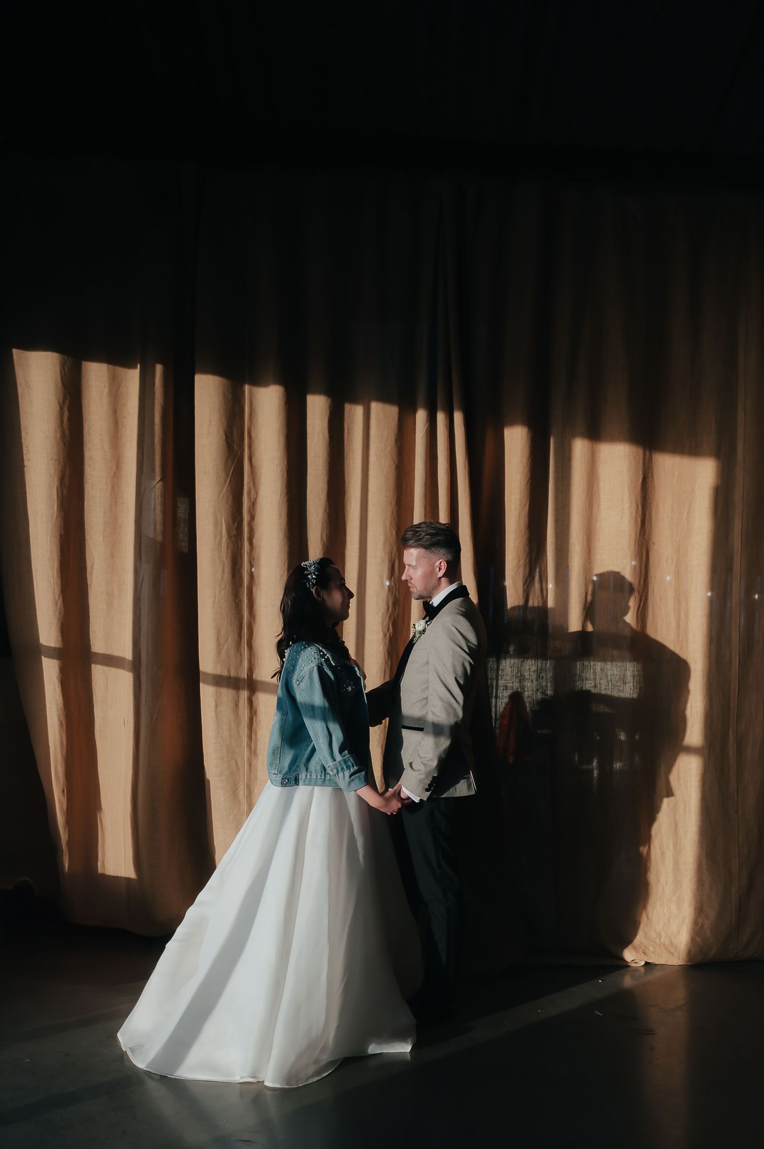 A dramatic silhouette of a couple against sunlit curtains in a wedding venue.