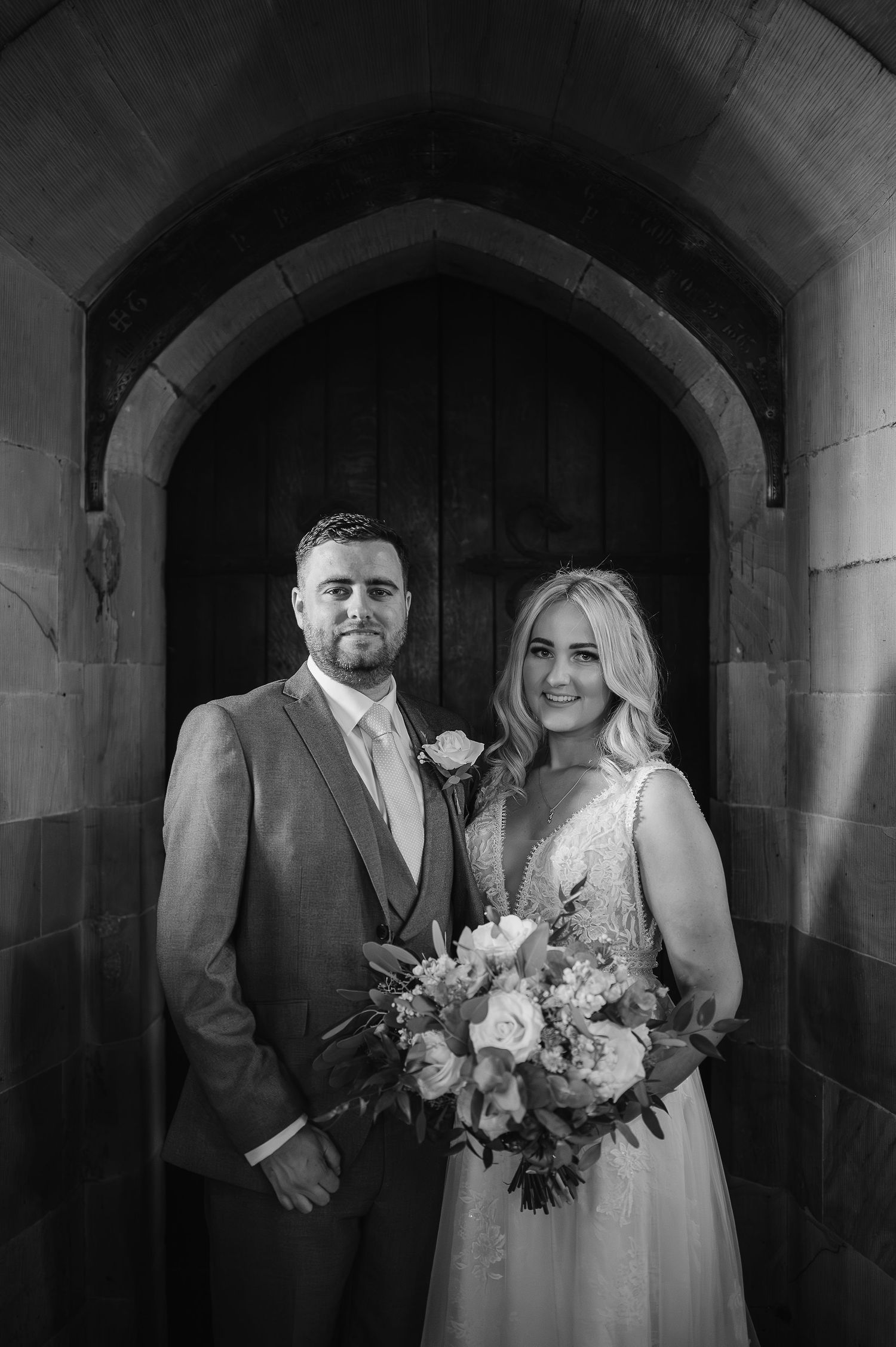 A classic wedding portrait of newlyweds standing under a stone archway.