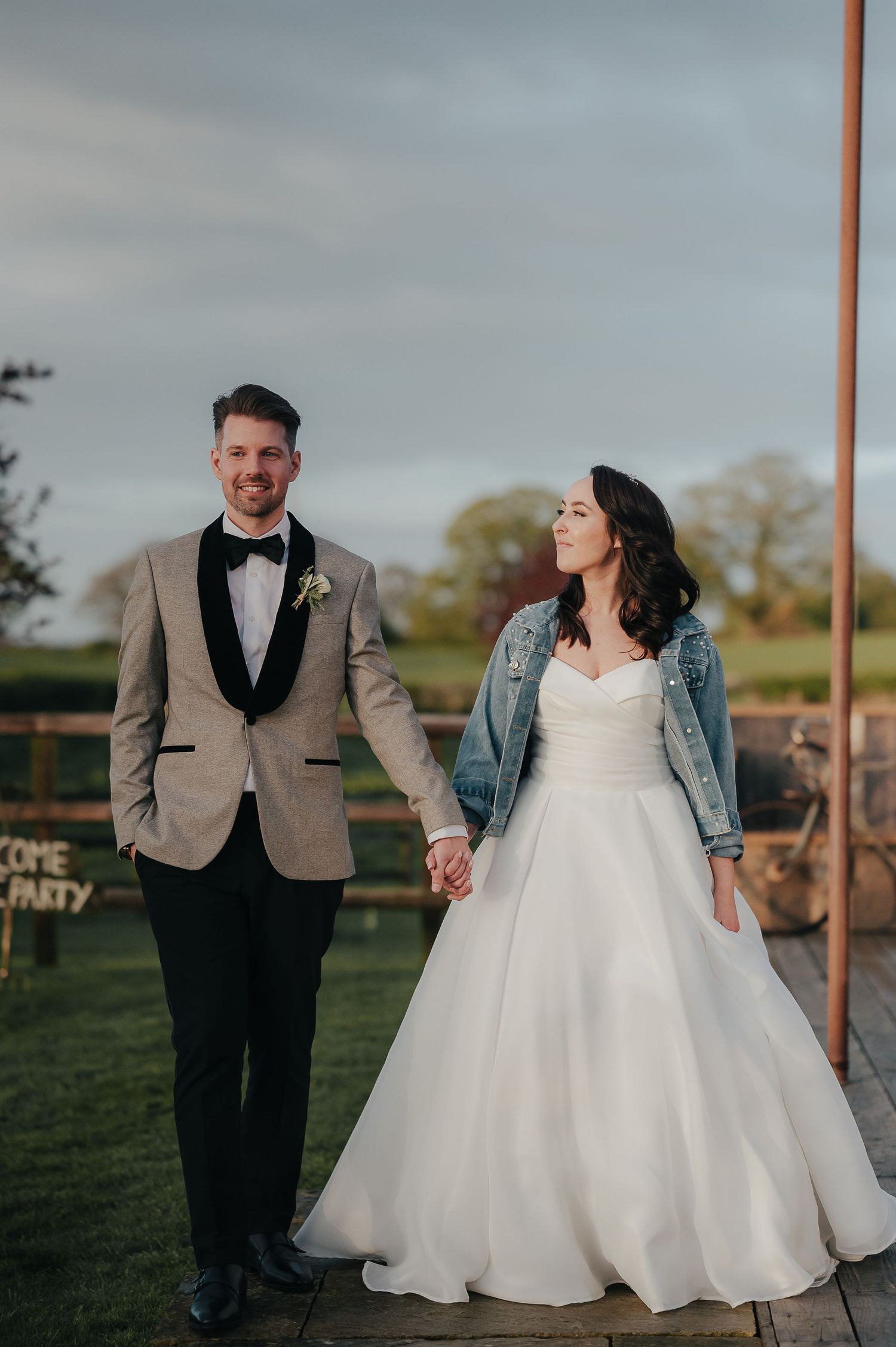 A couple poses outdoors in wedding attire with a denim jacket accent.