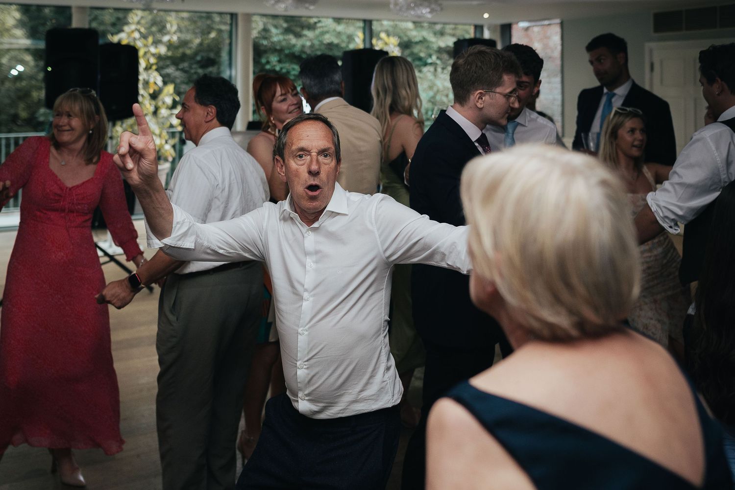 Party guests dancing energetically at a wedding reception with a person in red dress visible.
