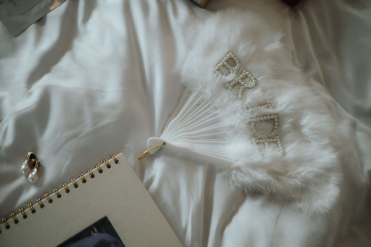 White feather detail on fabric with delicate embroidery and a spiral notebook.