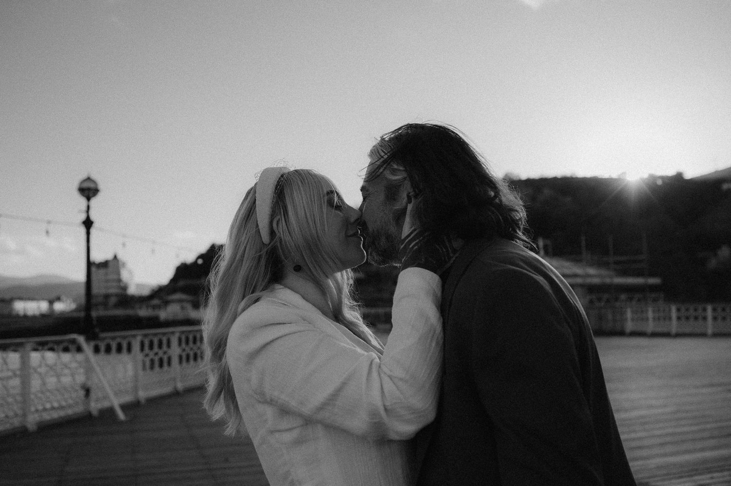 A romantic black and white photo of two people sharing an intimate moment on a boardwalk at dusk. North Wales Wedding .