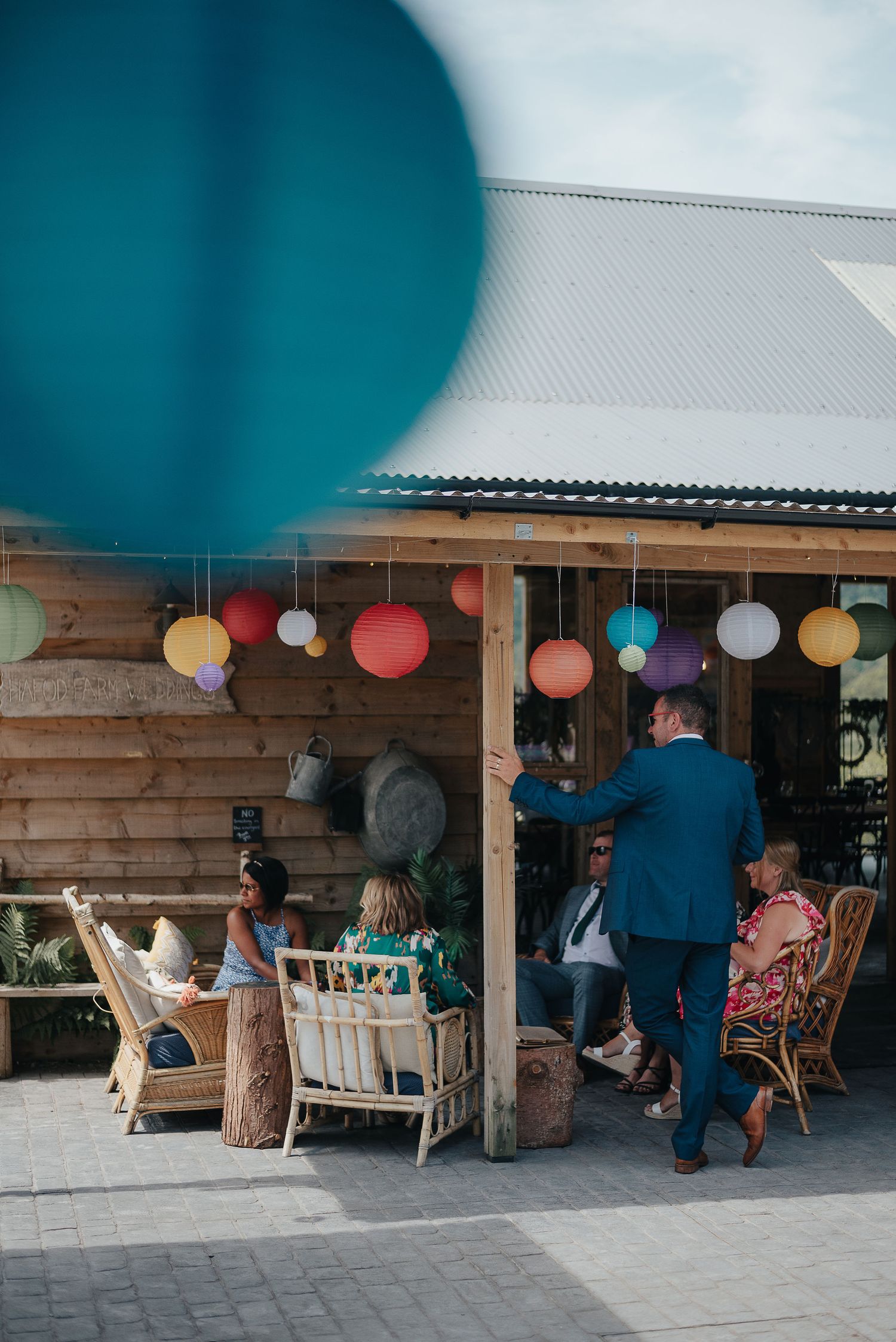 Outdoor wedding reception area with colorful paper lanterns and rustic wooden furniture.