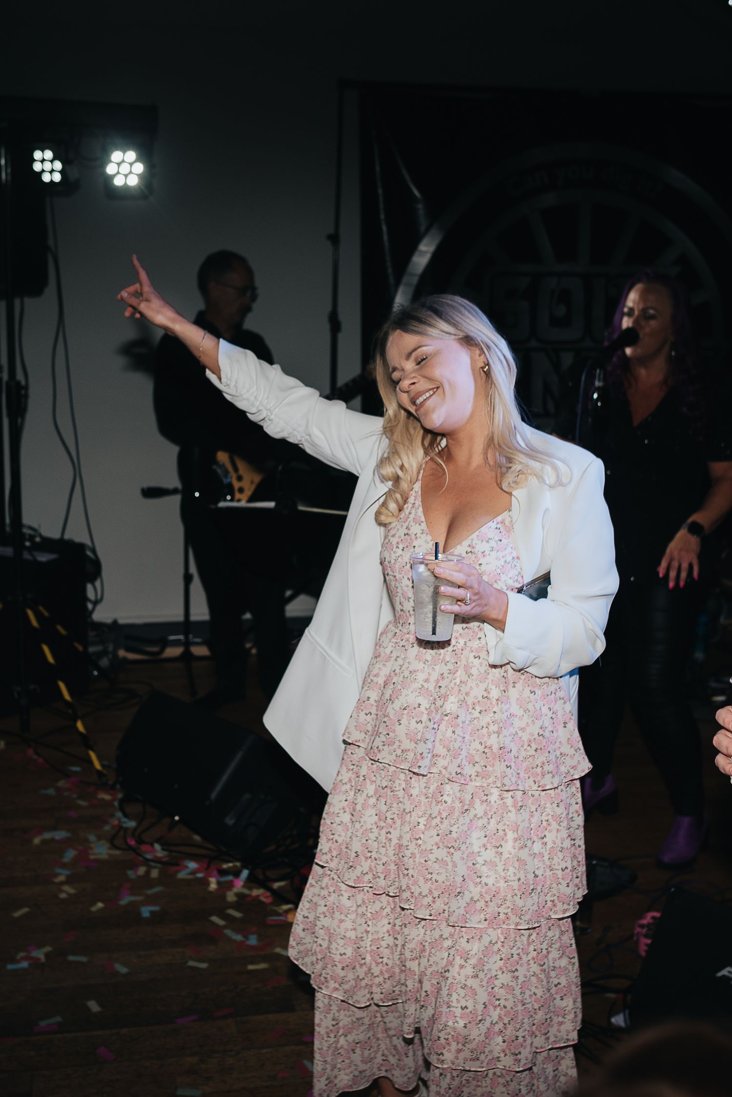 Guest dancing enthusiastically at wedding reception while wearing floral dress and white jacket.