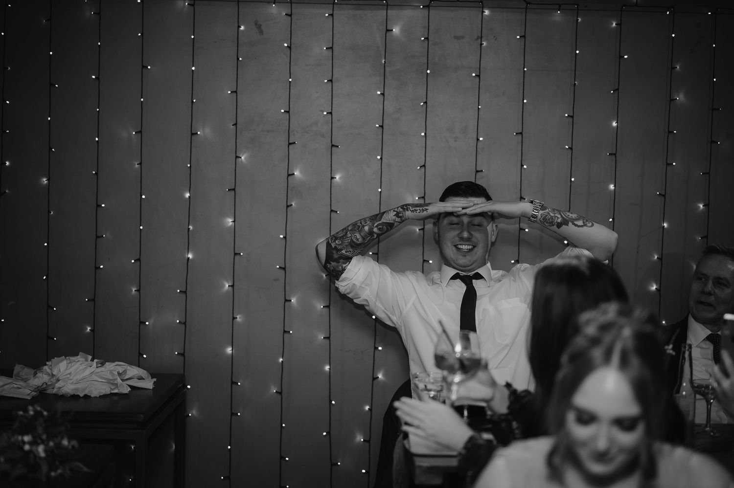 Black and white photo of wedding reception with twinkle lights in background.