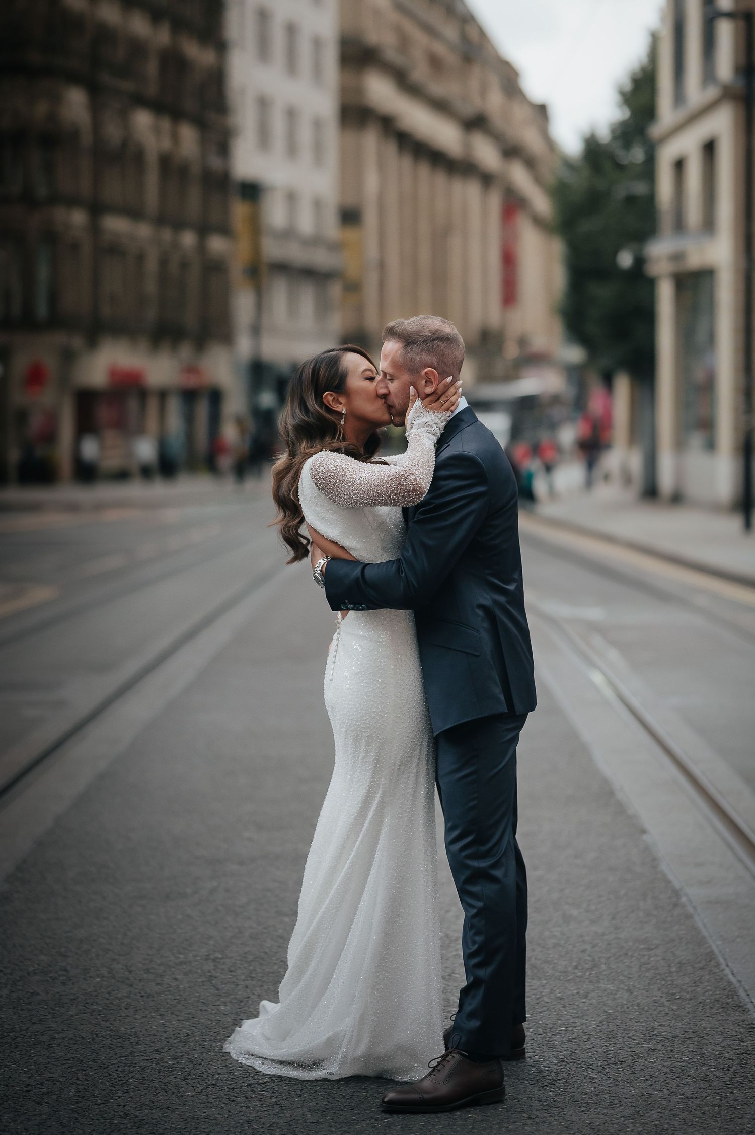 Romantic wedding couple embracing on urban street with historic architecture in background.
