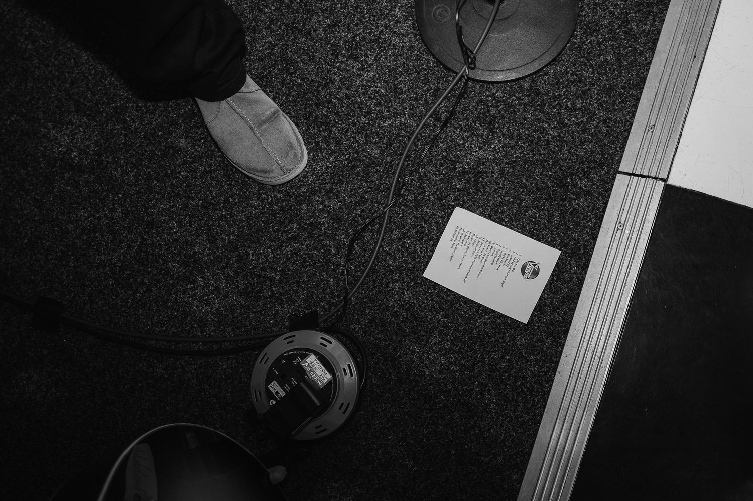 Top-down black and white shot of shoes and objects on a dark carpeted floor.