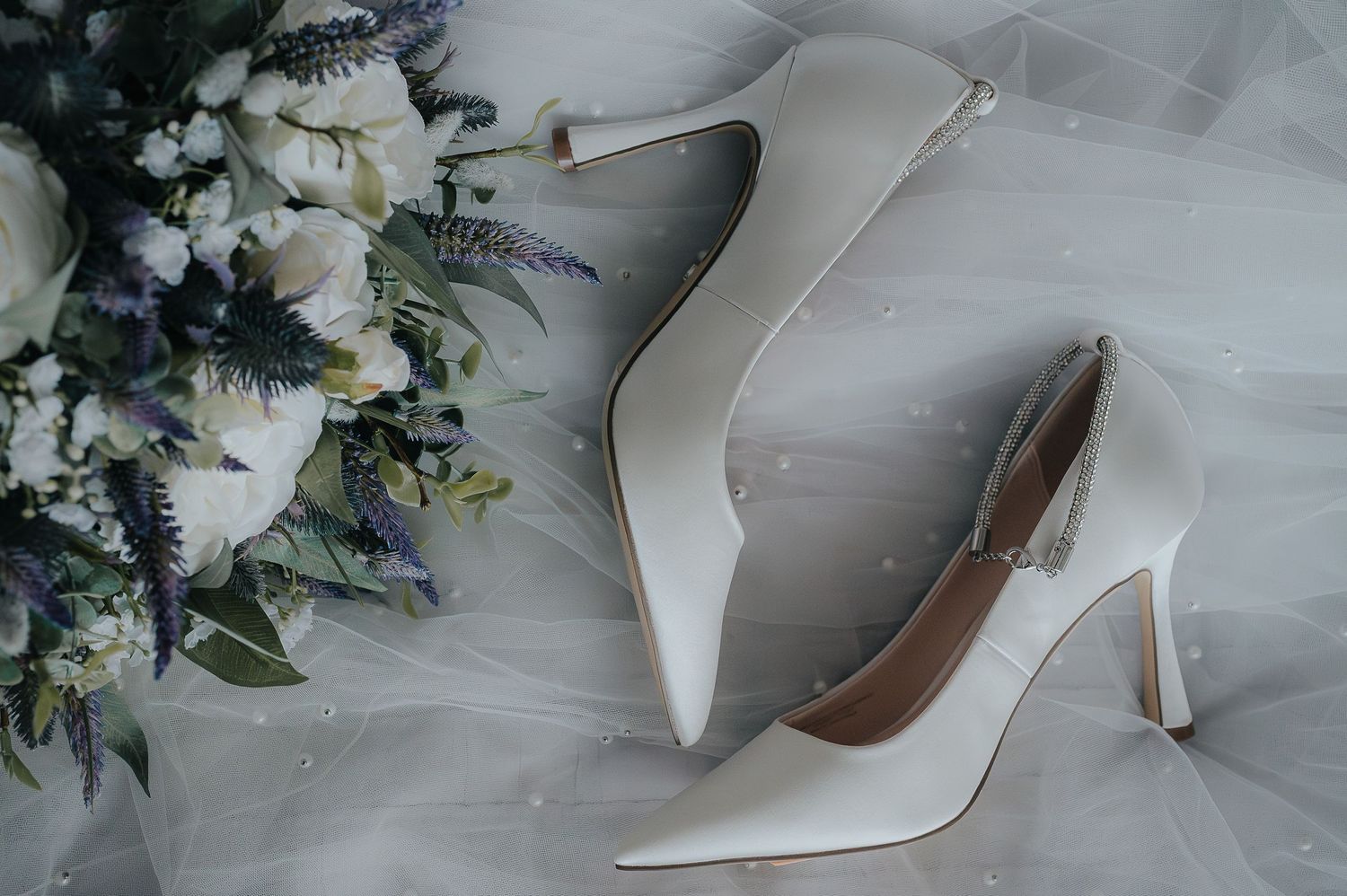 White bridal heels next to delicate floral arrangement with roses and lavender.
