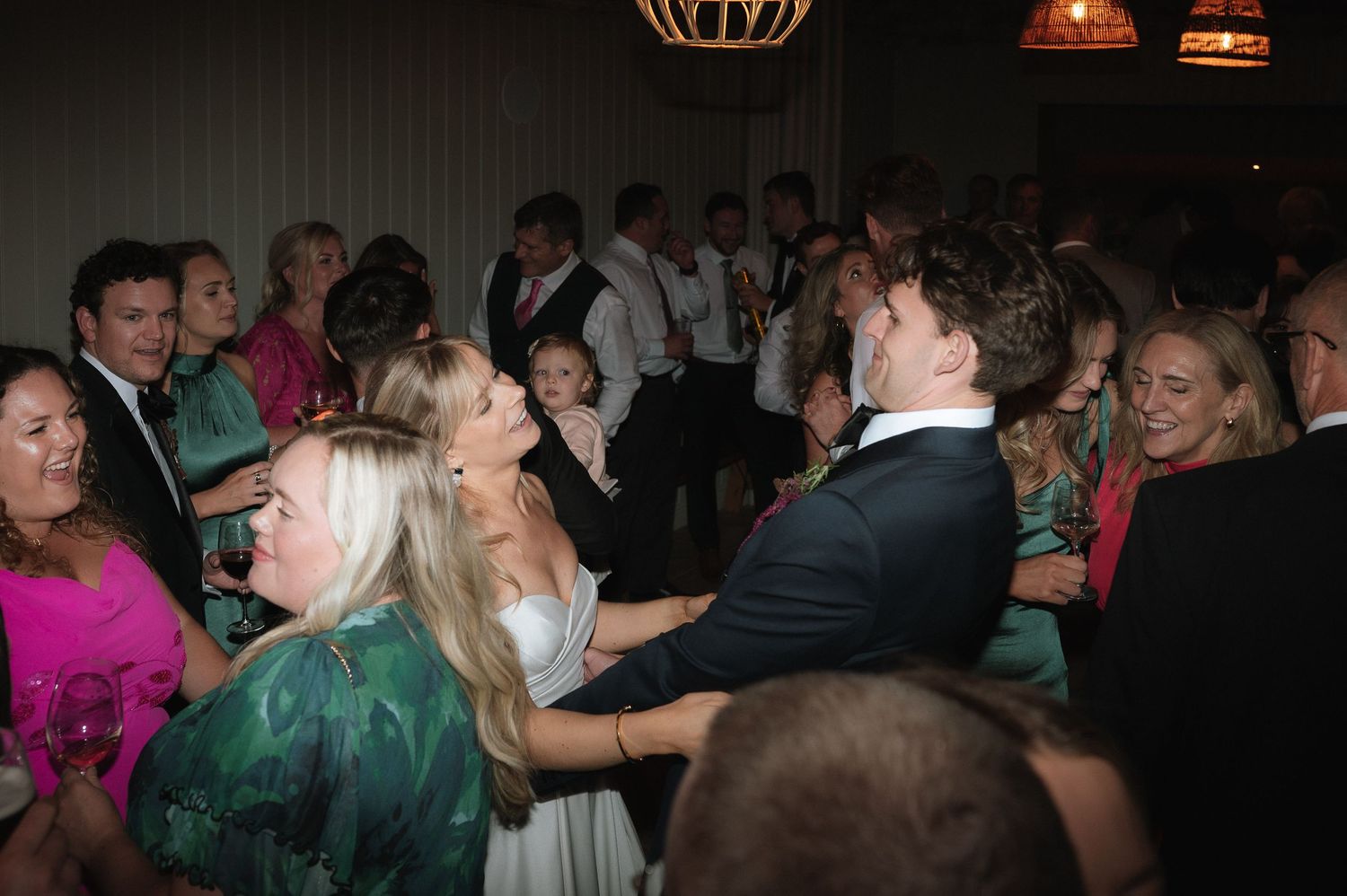 Wedding reception dance floor filled with guests celebrating in a dimly lit venue.