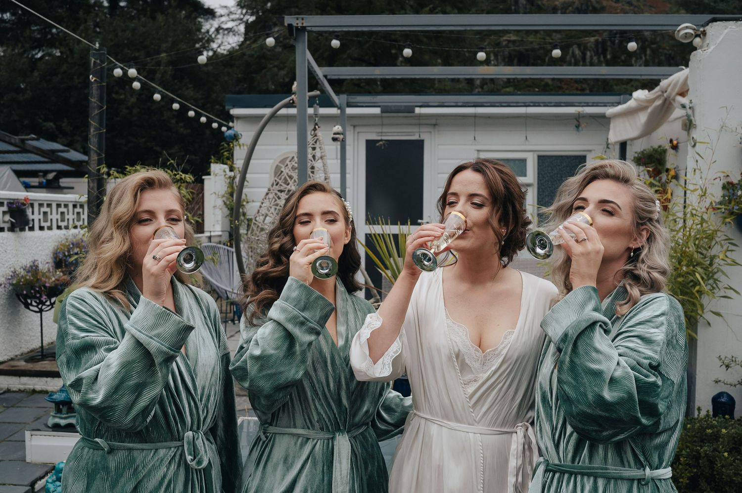 Group taking celebratory drinks together outdoors wearing sage green and white attire.