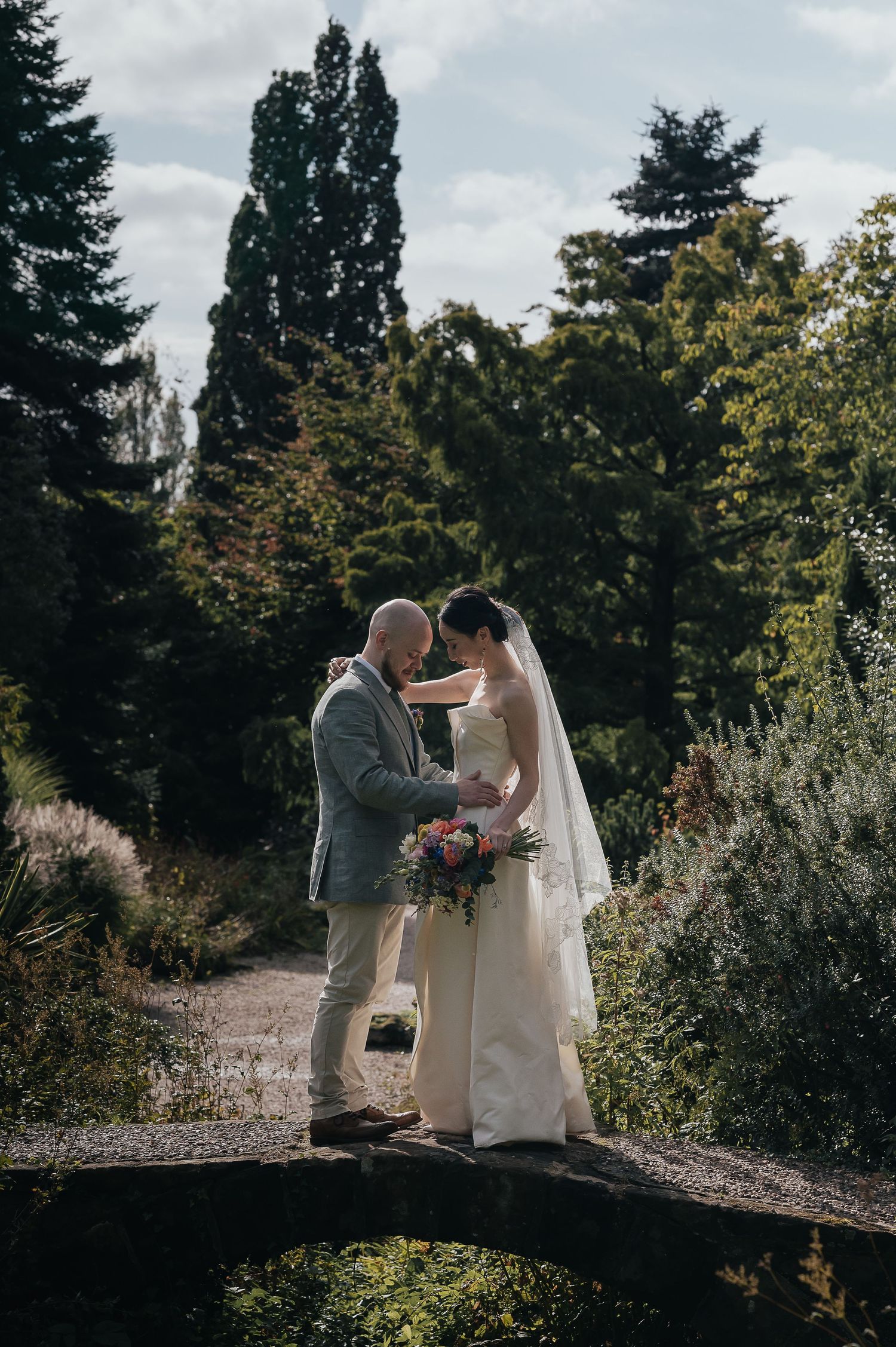 Couple shares intimate moment on stone bridge during outdoor wedding photoshoot.