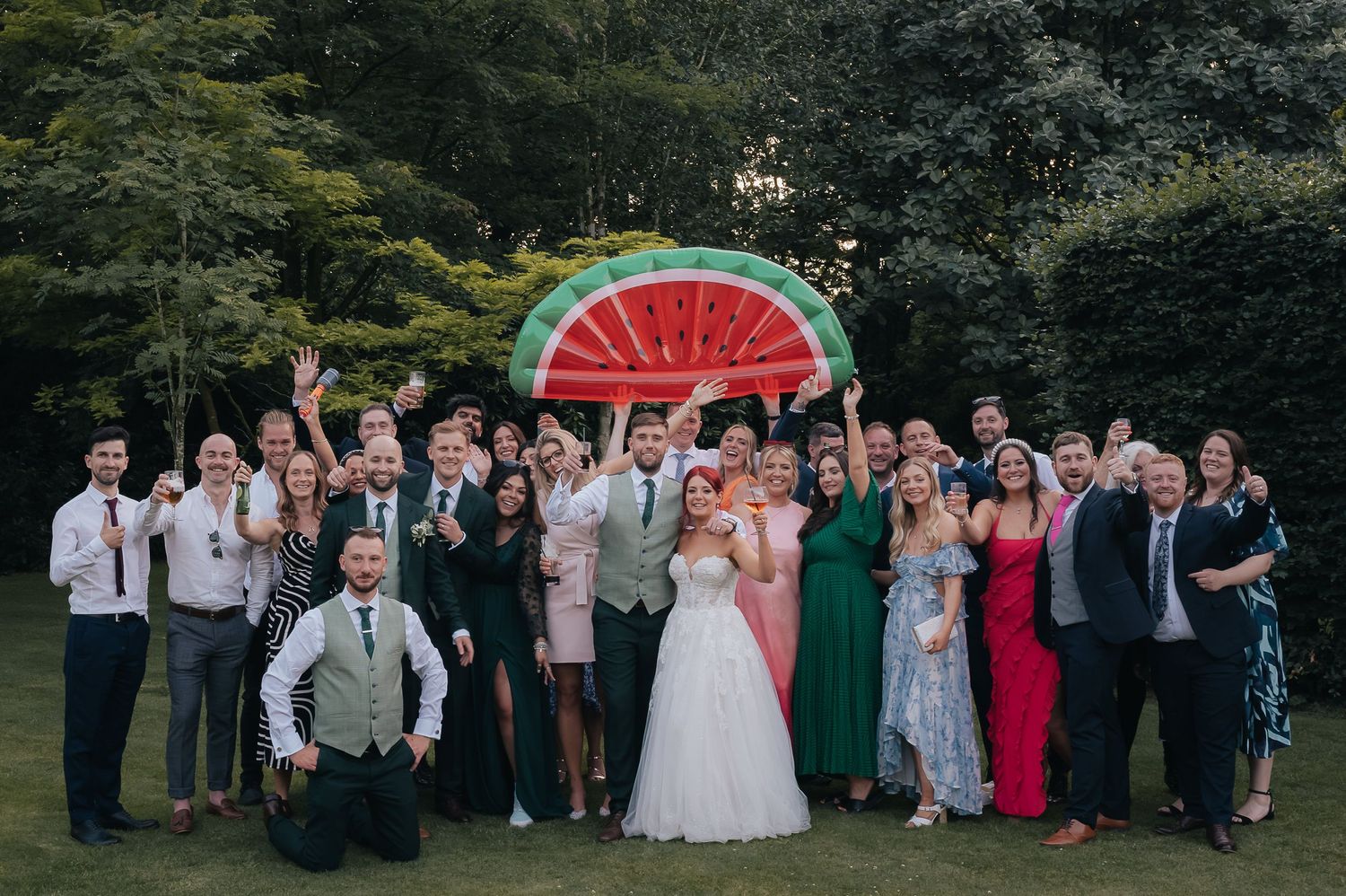 Wedding party poses for a group photo in front of a decorative watermelon backdrop.