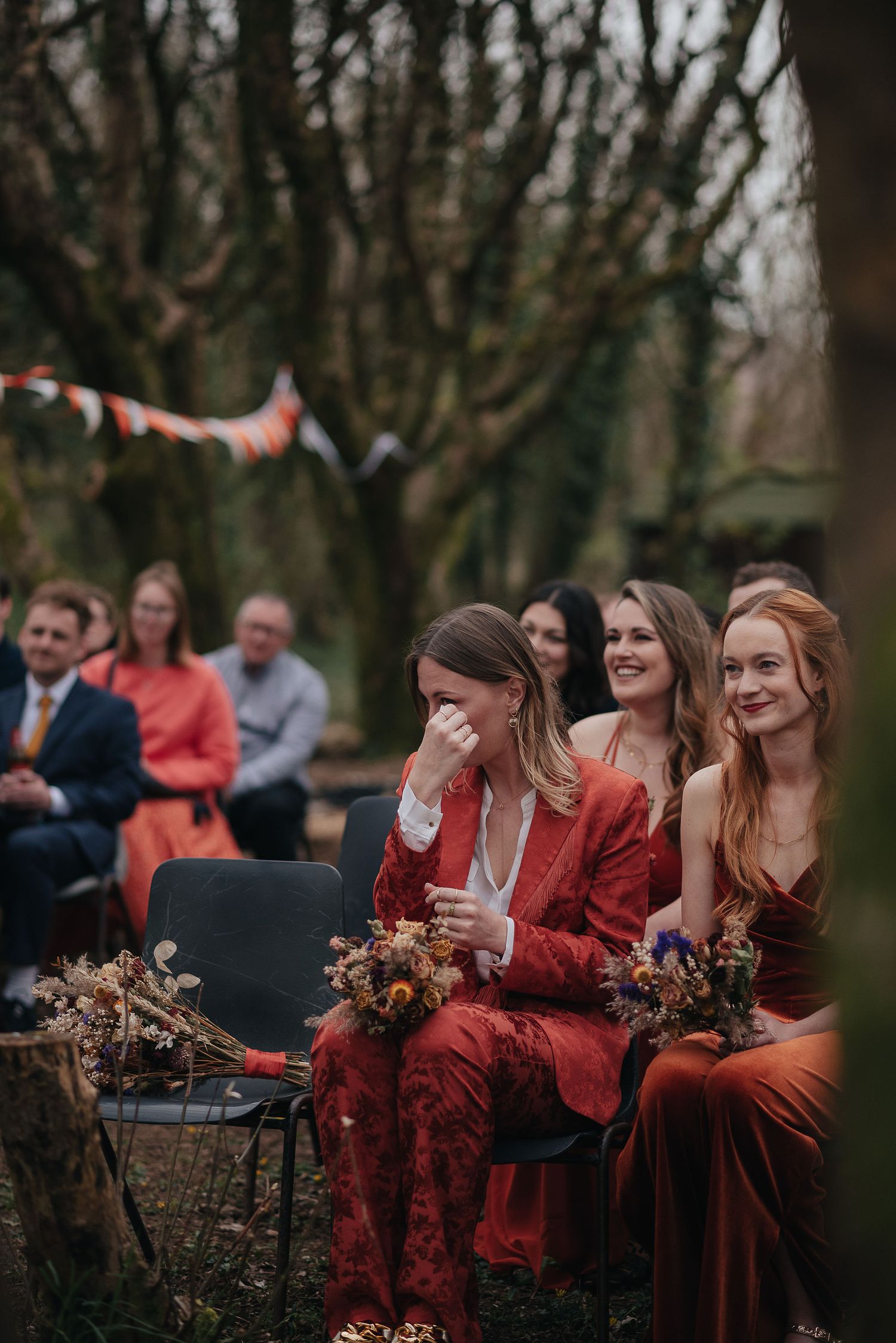 Wedding guests in red attire sitting outdoors watching an emotional ceremony.