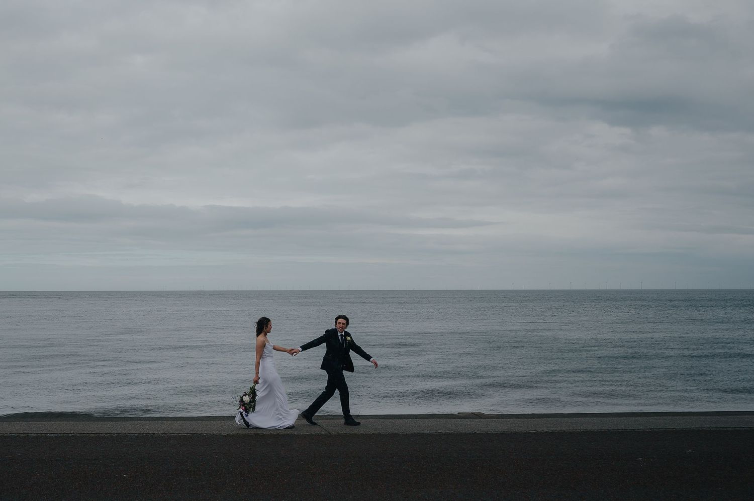 Silhouetted couple holding hands while walking along a misty beach.