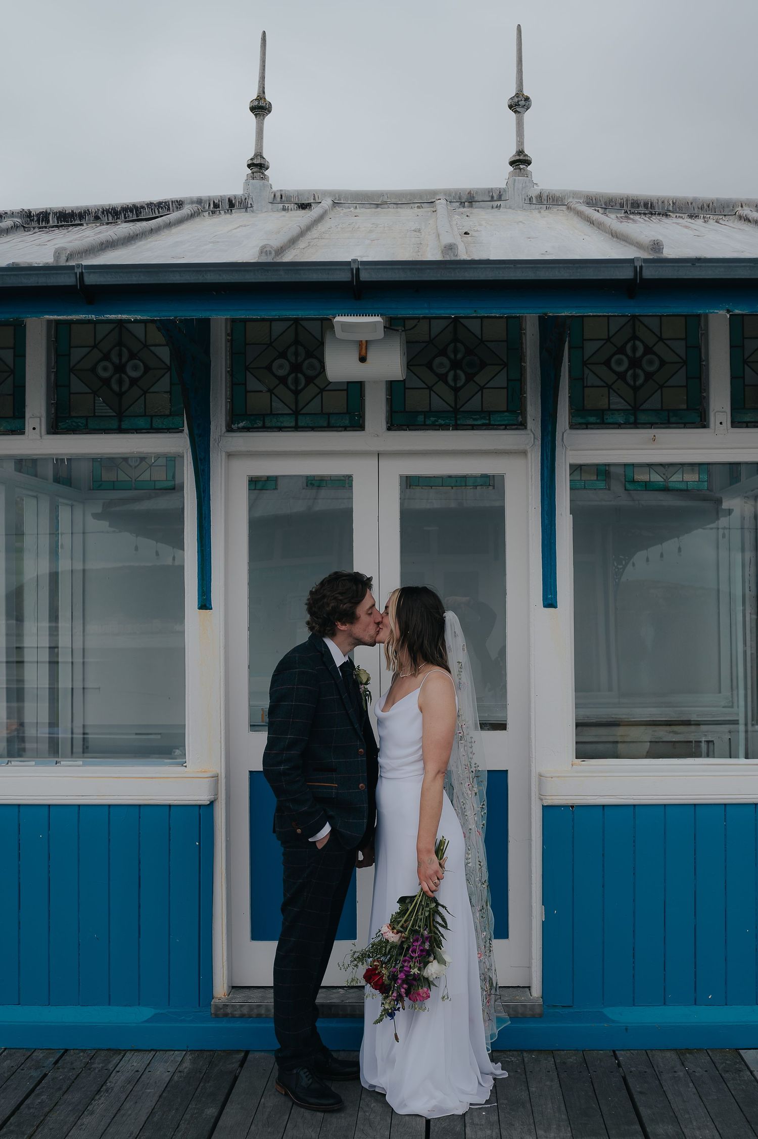 Wedding couple sharing an intimate moment against blue and white Victorian seaside architecture.