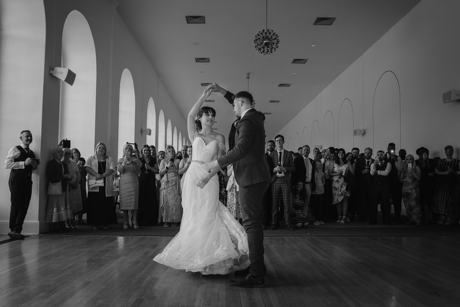 A couple sharing their first dance in an elegant white-walled venue with arched windows.