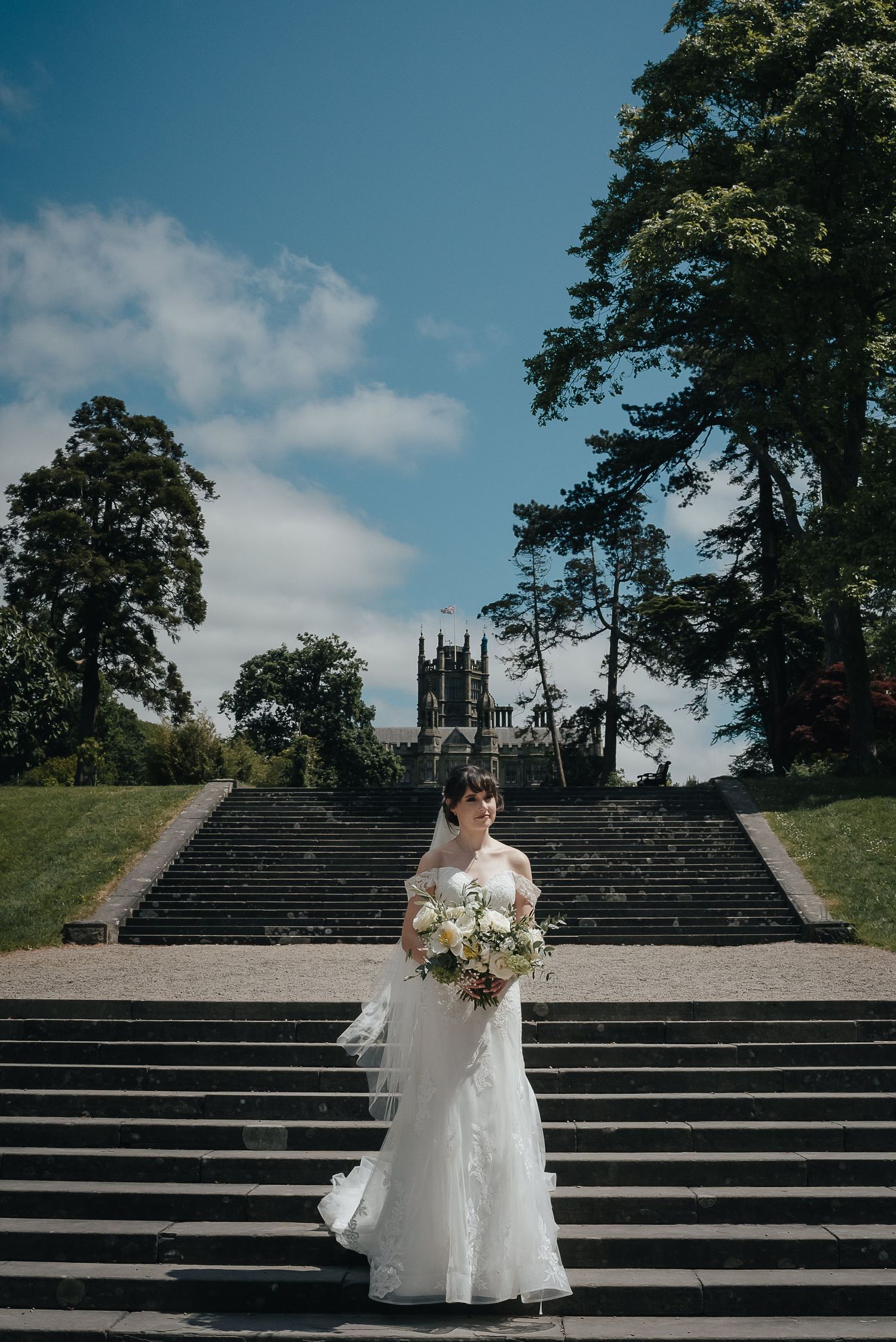 Grand stone staircase leads to Gothic church spires framed by tall trees against blue sky.