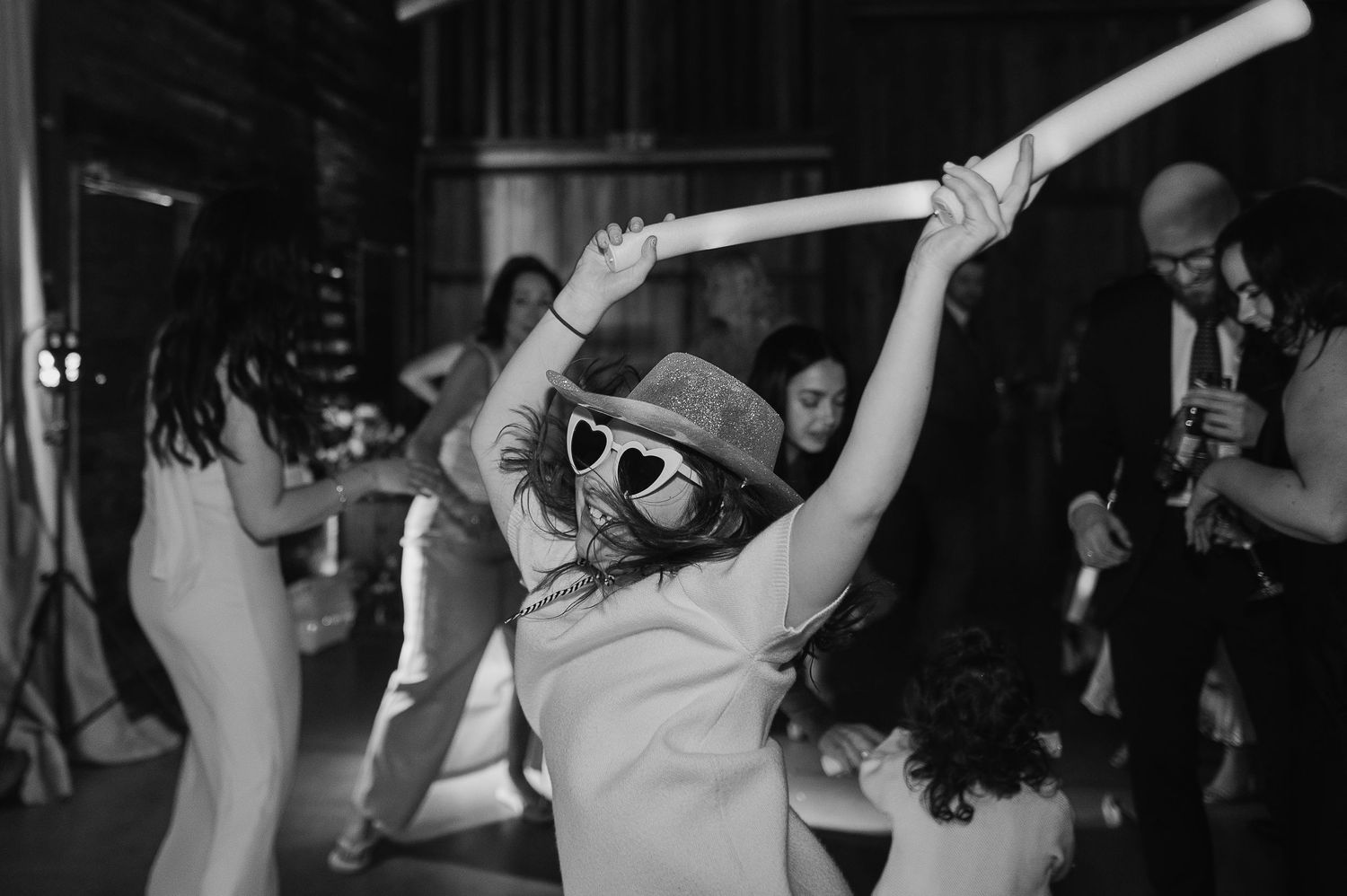 Wedding guest in sunglasses joyfully dancing with light-up foam sticks at reception.