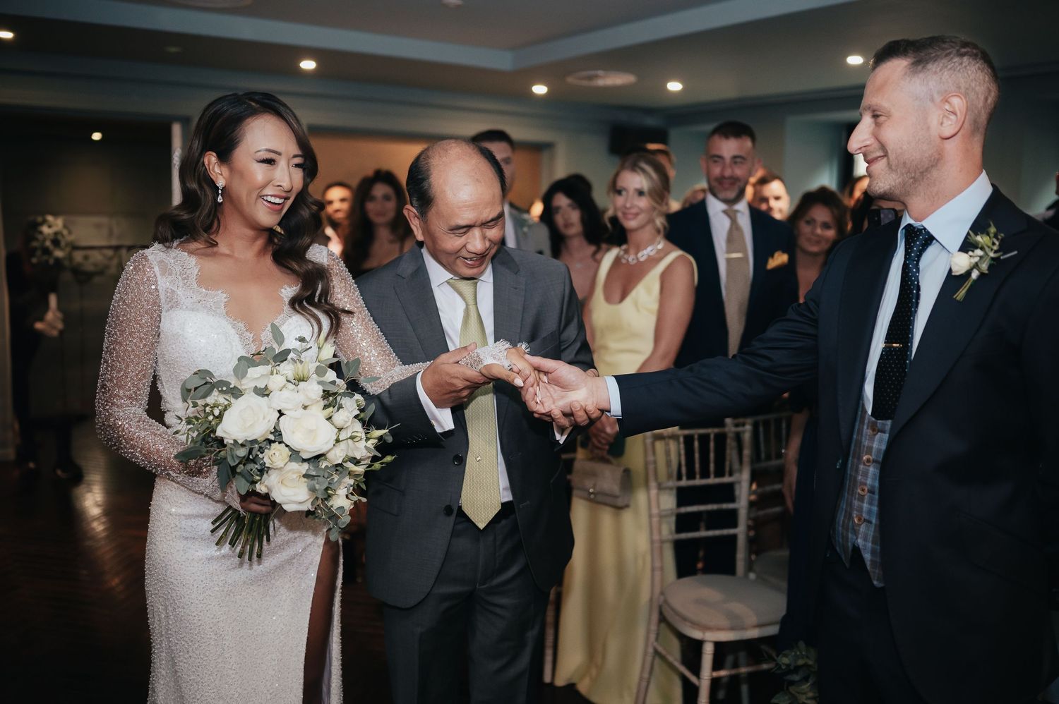 Wedding ceremony moment with bouquet of white flowers and guests watching in formal attire.