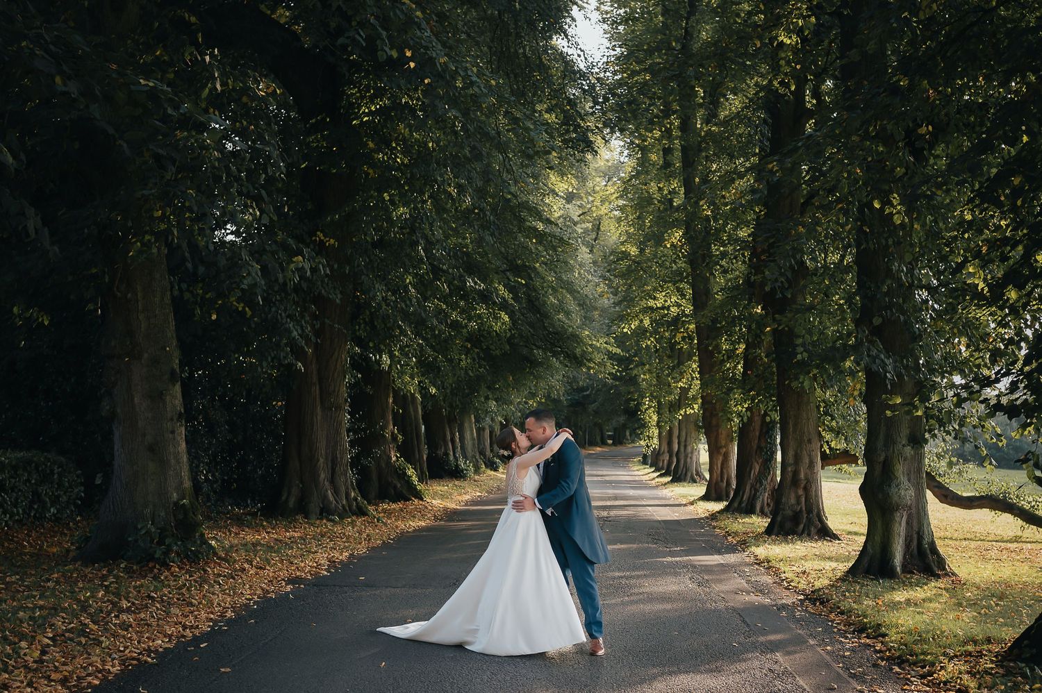 A couple shares a romantic moment on a tree-lined path during autumn wedding photography.