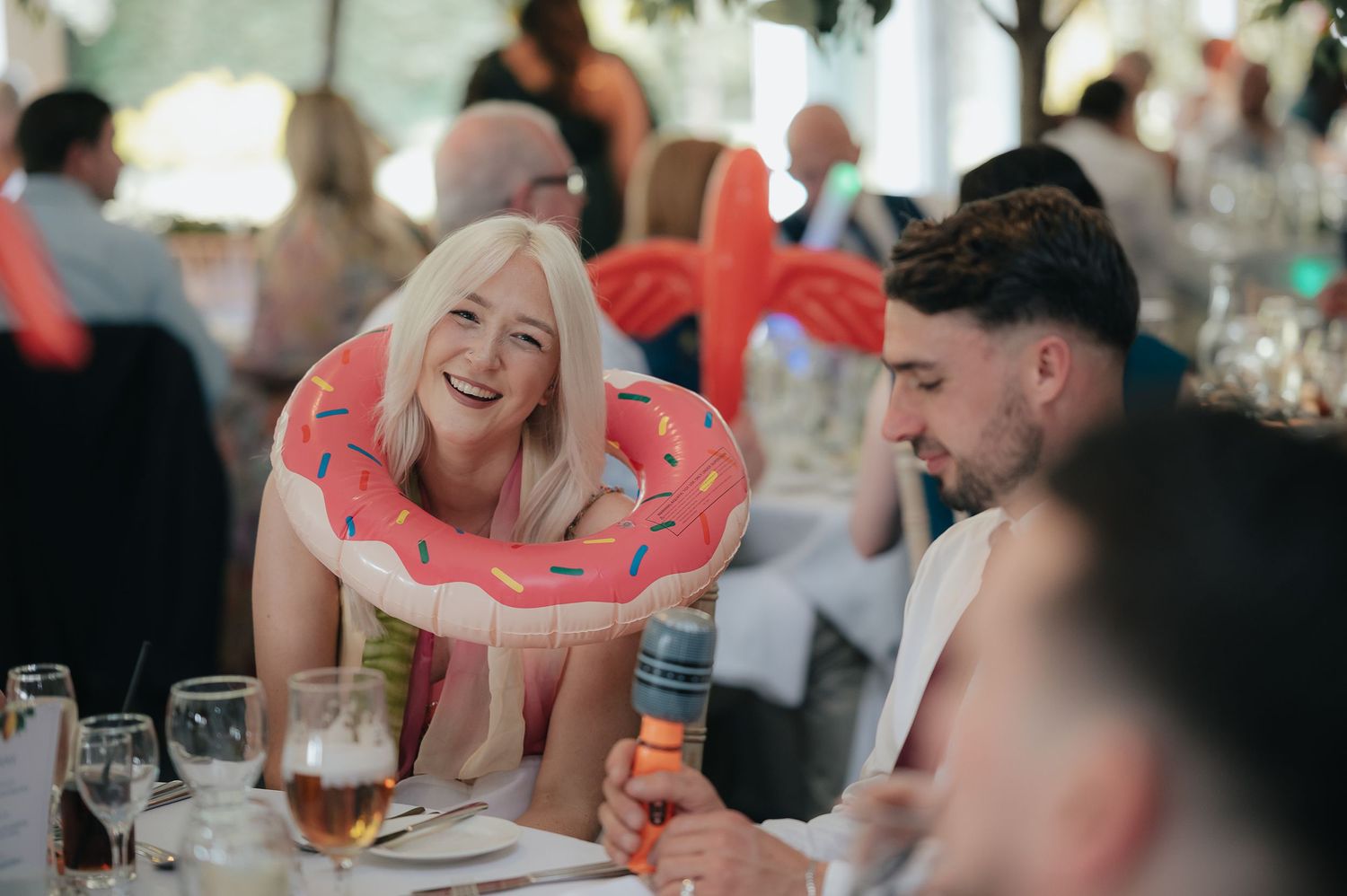 Wedding guest wearing inflatable pool float ring laughs at reception table.