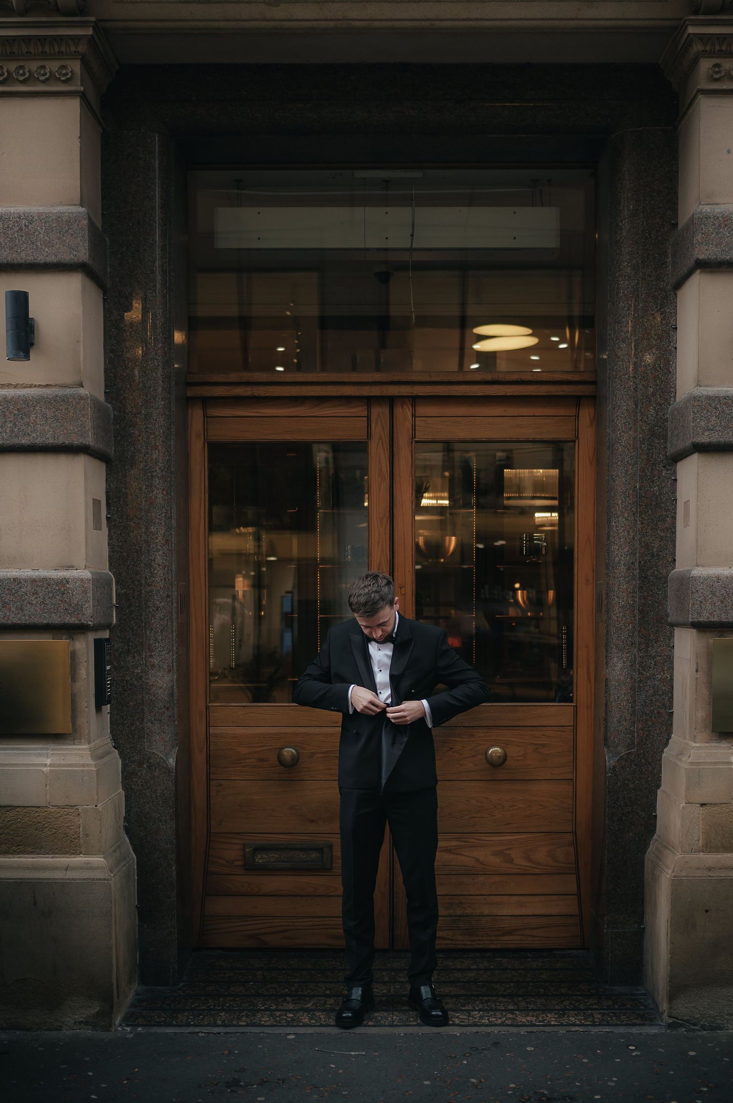 A man in a dark suit reads a document while standing in a doorway of a historic stone building.