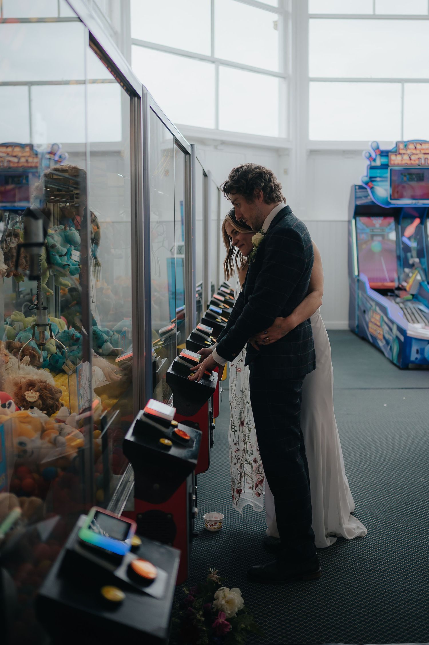Wedding couple playing claw machine game at an arcade.