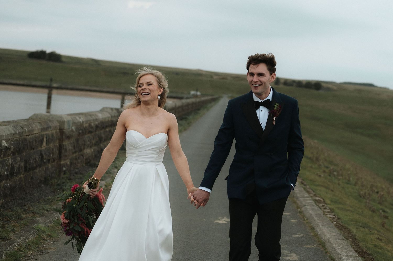 Couple walking together on a countryside path surrounded by rolling hills and green landscapes.