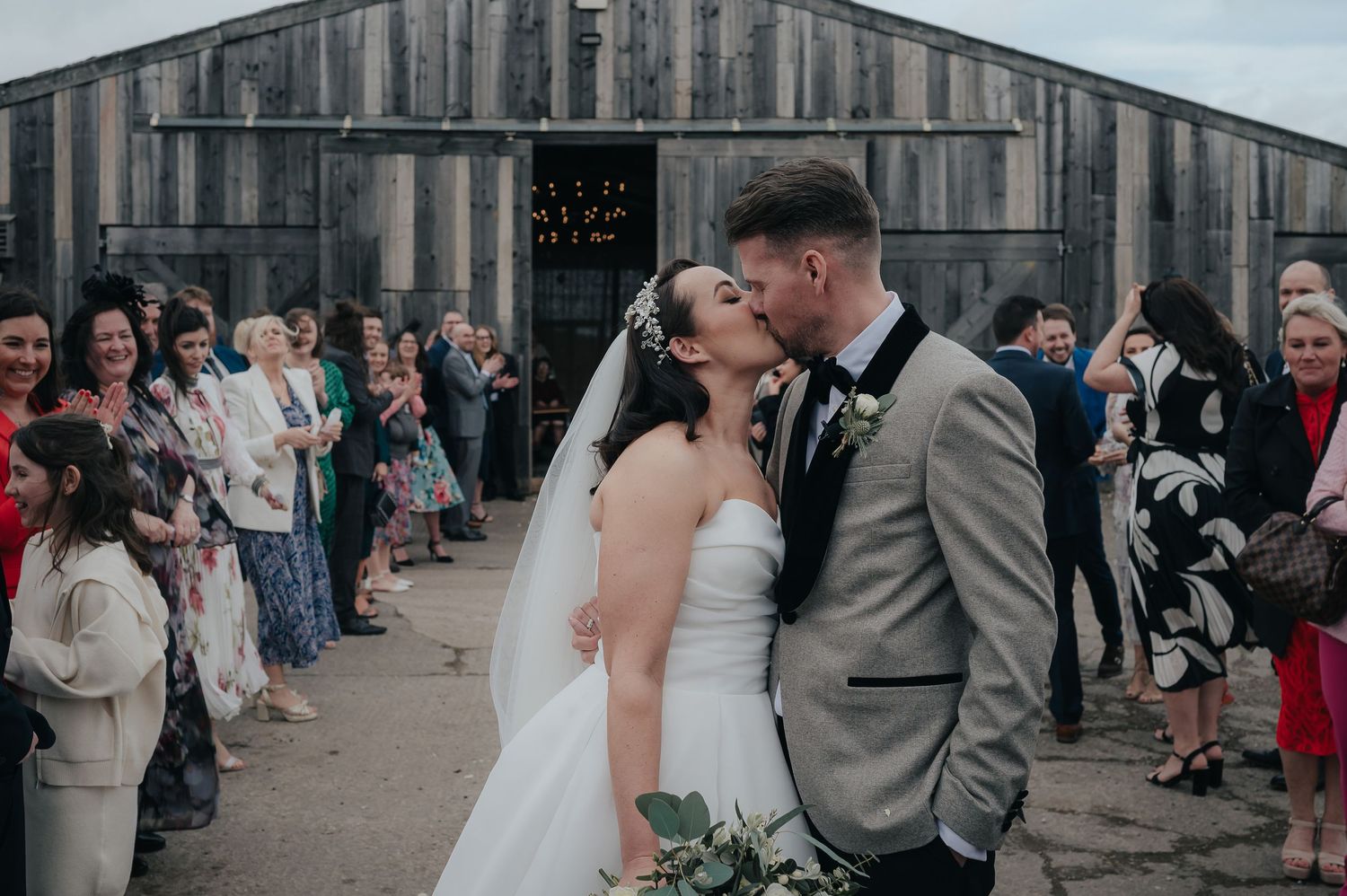 A couple shares their first kiss as newlyweds outside a rustic barn venue.