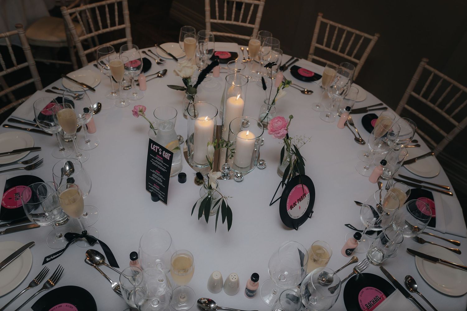Elegant white wedding reception table settings with glowing candles and floral centerpieces at multiple round banquet tables.