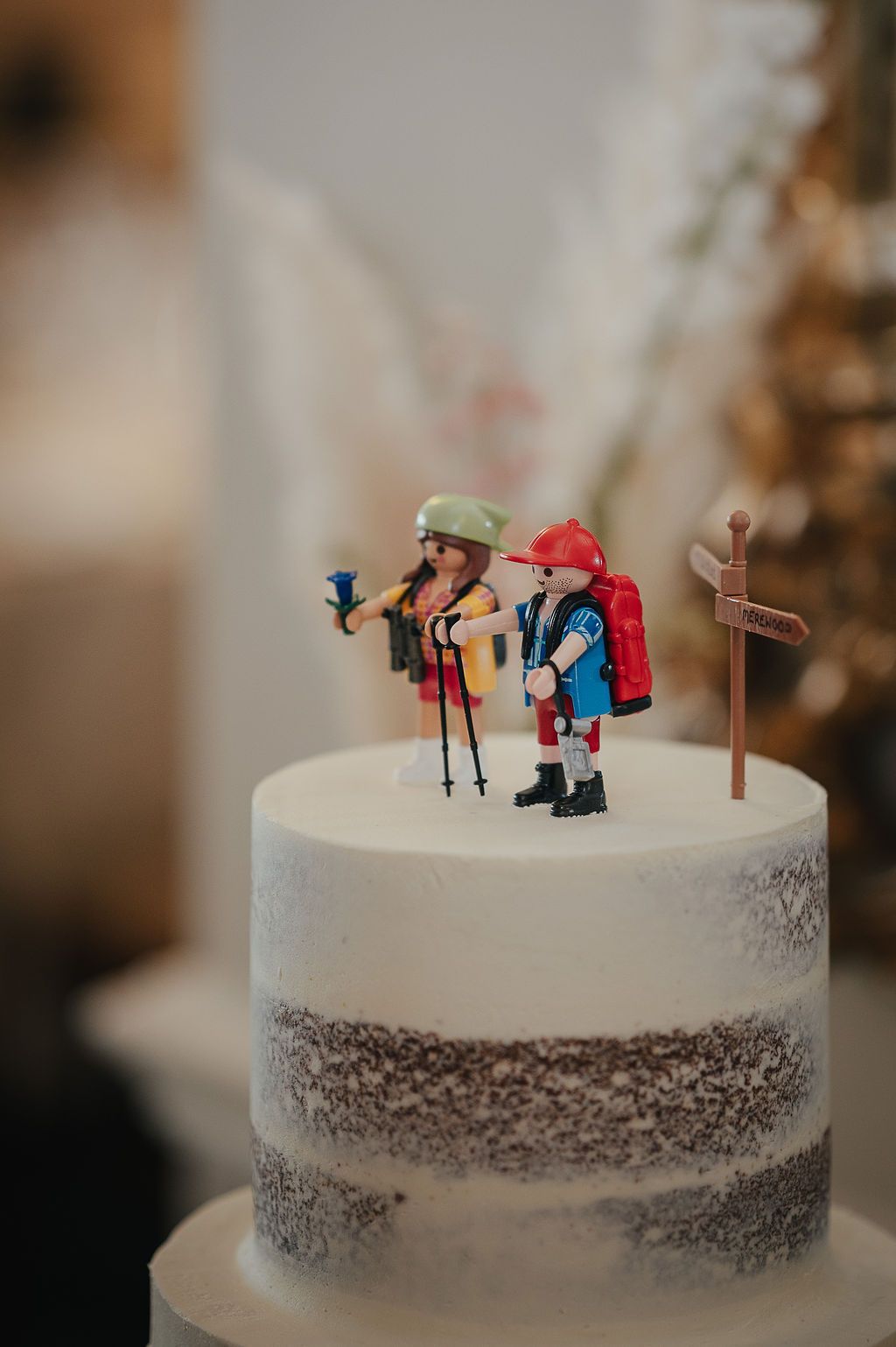 White wedding cake decorated with hiking themed figurine toppers and trail signpost.