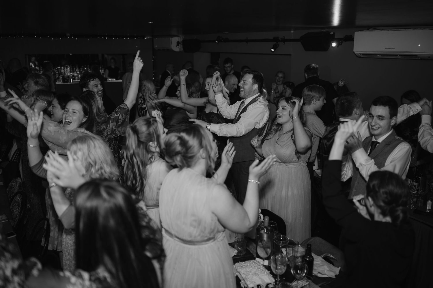 Wedding reception dance floor filled with guests celebrating in black and white photography.