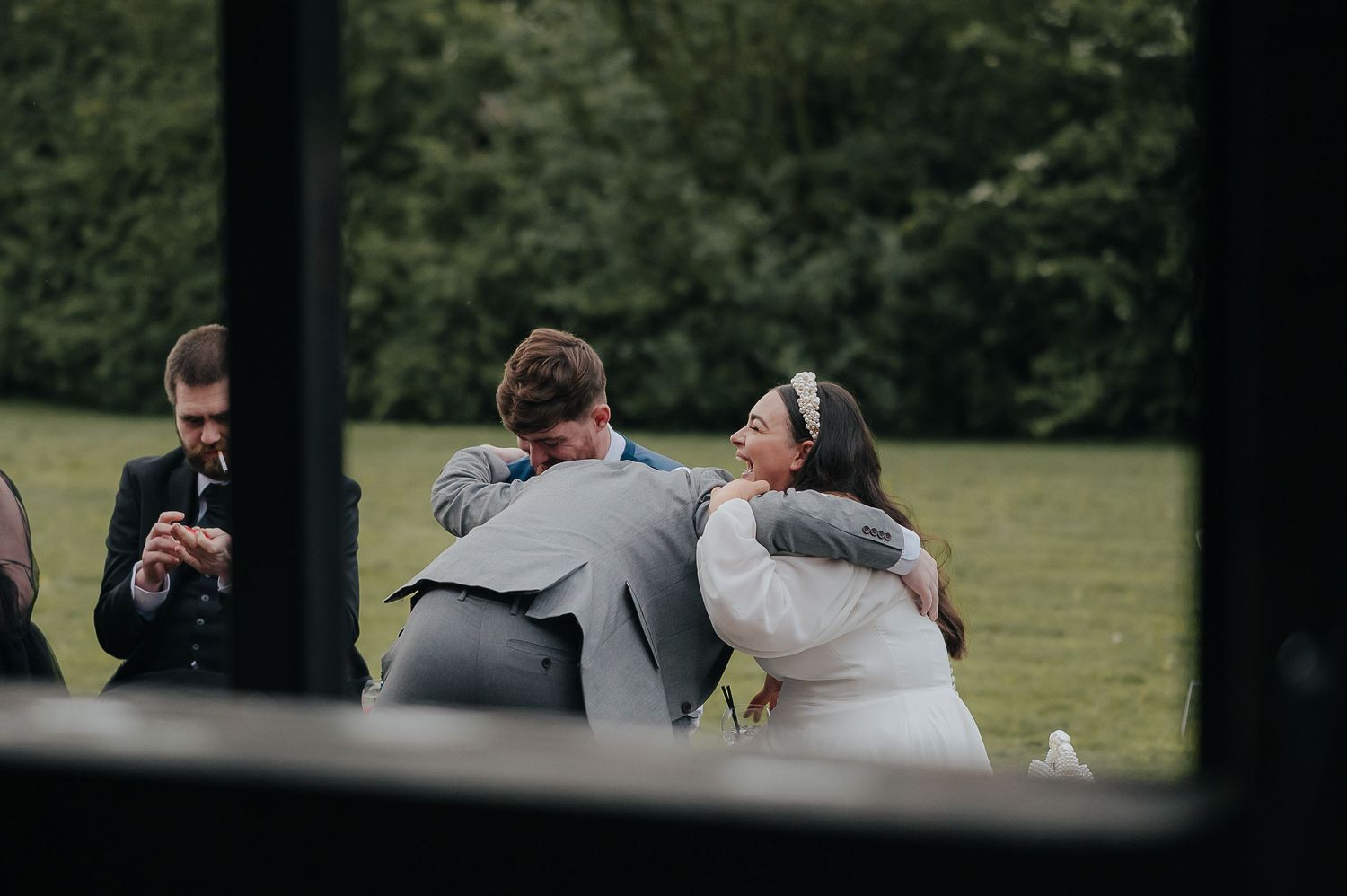 Wedding guests embracing outdoors viewed through a window frame.